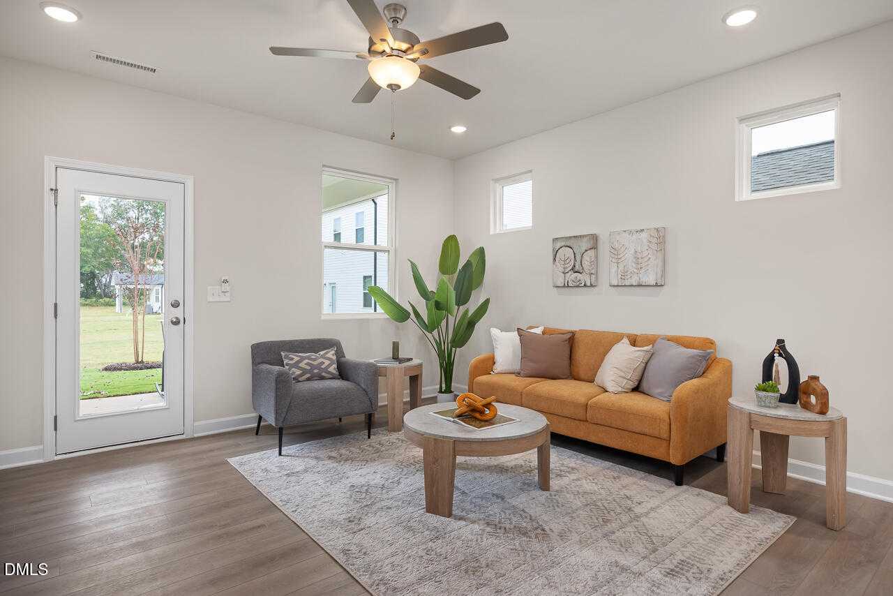 Cozy living room with orange sofa, gray armchair, ceiling fan, and backyard view via glass door in Davidson Homes The Carter C, Lillington, NC