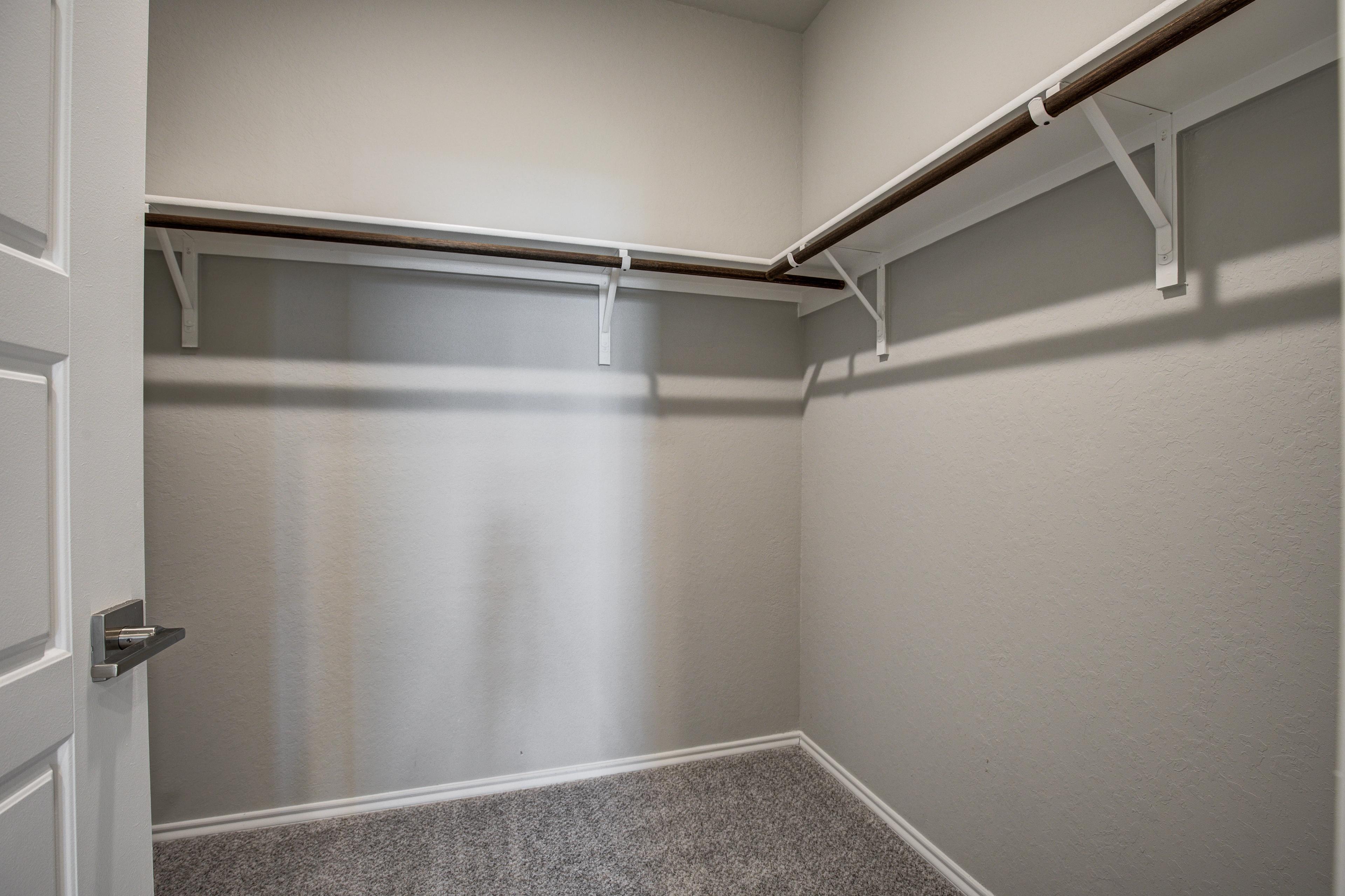 Spacious walk-in closet in The Asheville master suite with custom wooden shelving, white brackets, and neutral beige walls