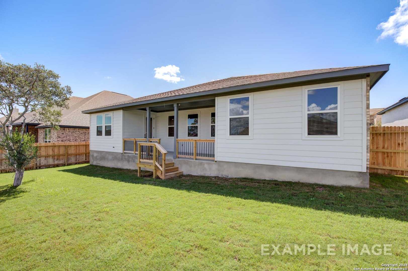 Back view of single-story Rockford G home featuring covered patio, wooden deck stairs, and fenced grassy yard in Ladera, San Antonio, Texas