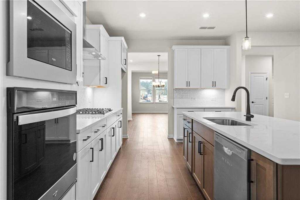 Spacious galley kitchen with white shaker cabinets, quartz island sink, stainless appliances in The Glenwood A by Davidson Homes, Loganville, GA