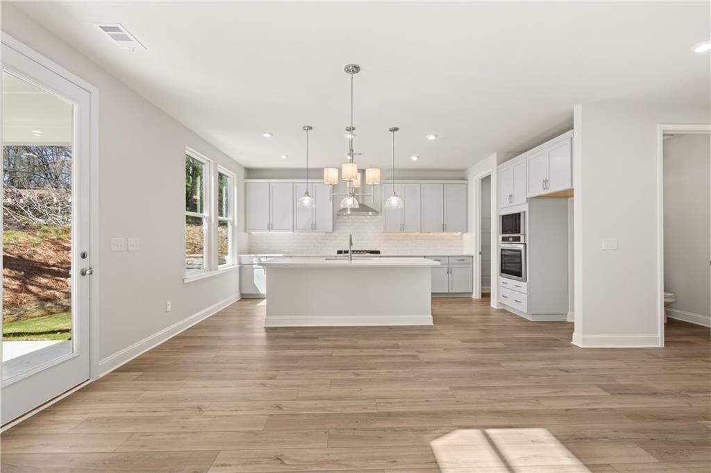 Modern white kitchen with large island, stainless appliances, pendant lights, and hardwood floors in The Danbury C, Buford, Georgia