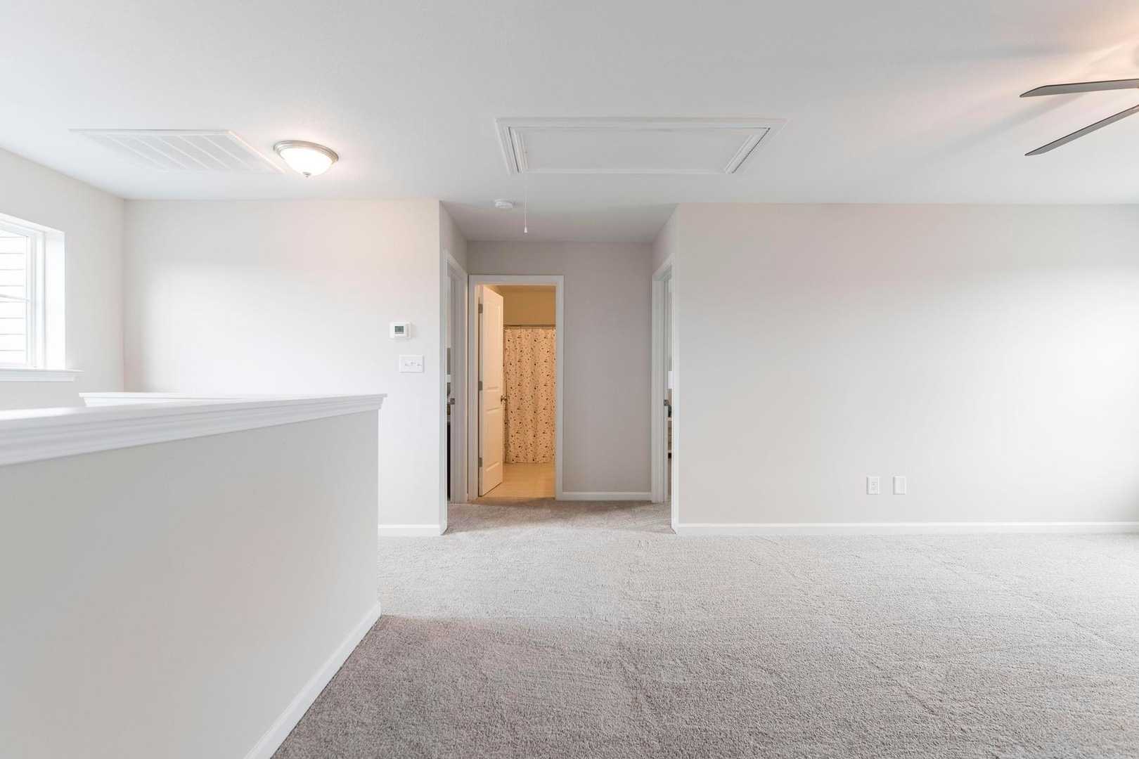Spacious upstairs loft with balcony overlook, carpeted floors, ceiling fan, and bathroom access at Cape Reserve at Donahue Ridge in Auburn Alabama