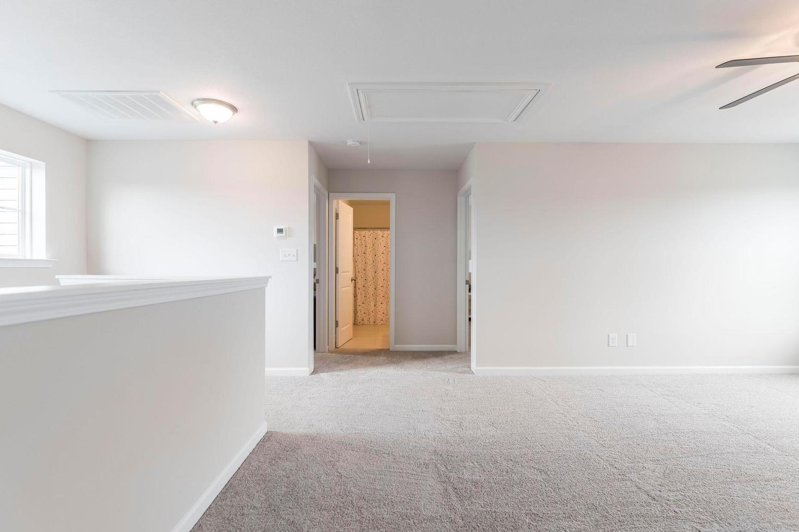 Spacious upstairs loft with balcony overlook, carpeted floors, ceiling fan, and bathroom access at Cape Reserve at Donahue Ridge in Auburn Alabama