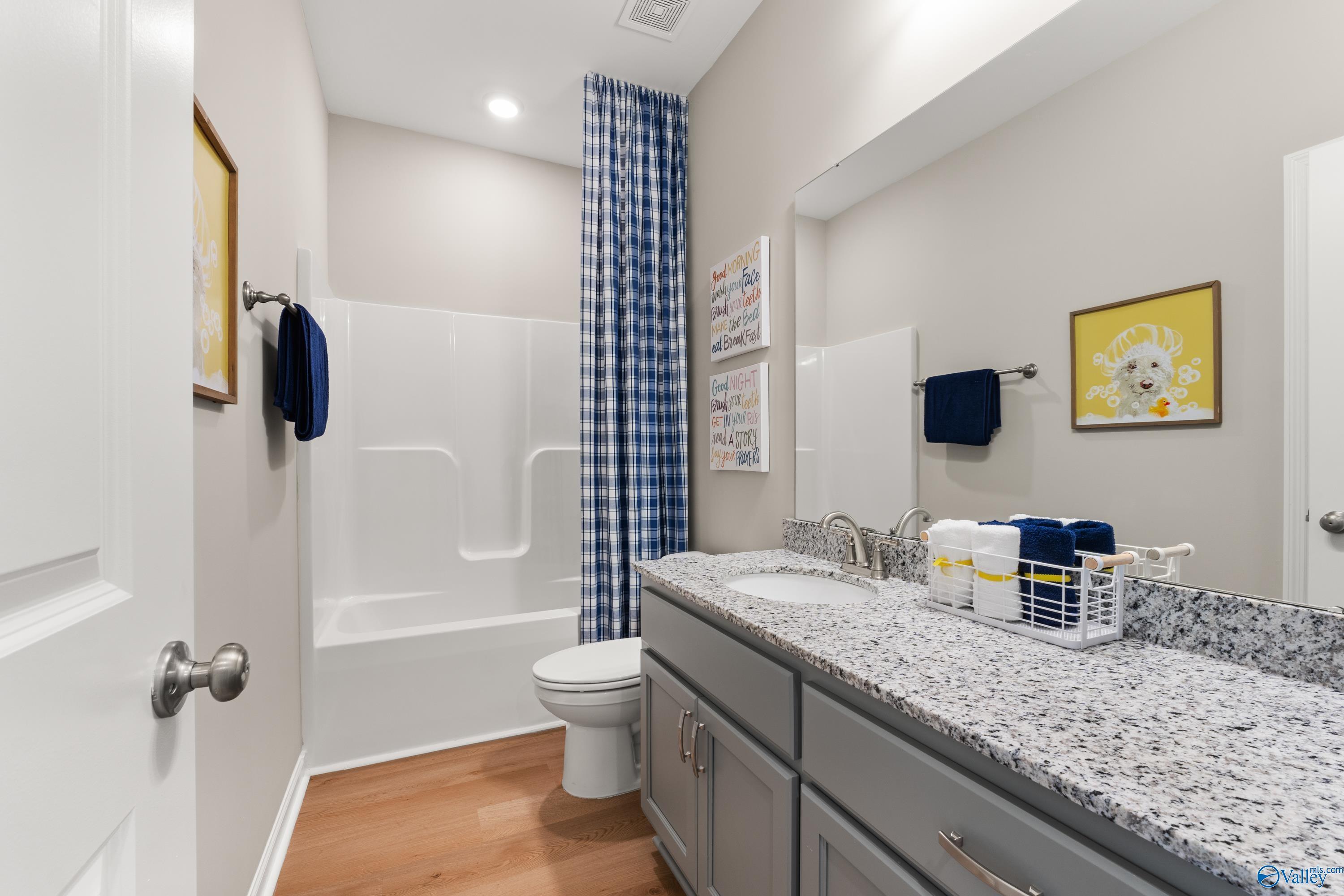 Modern bathroom with granite vanity, tub-shower combo, blue striped curtain, and gray cabinets in Davidson Homes The Sanctuary, Athens AL