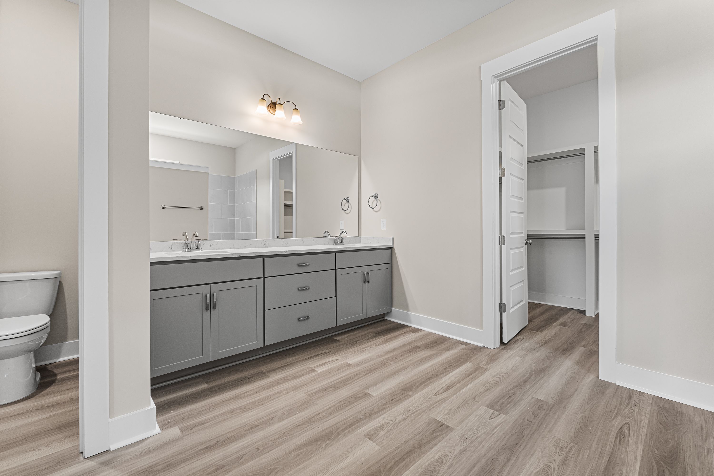 Spacious master bathroom in The Oxford A featuring double gray vanity, beige walls, wood flooring, and walk-in closet