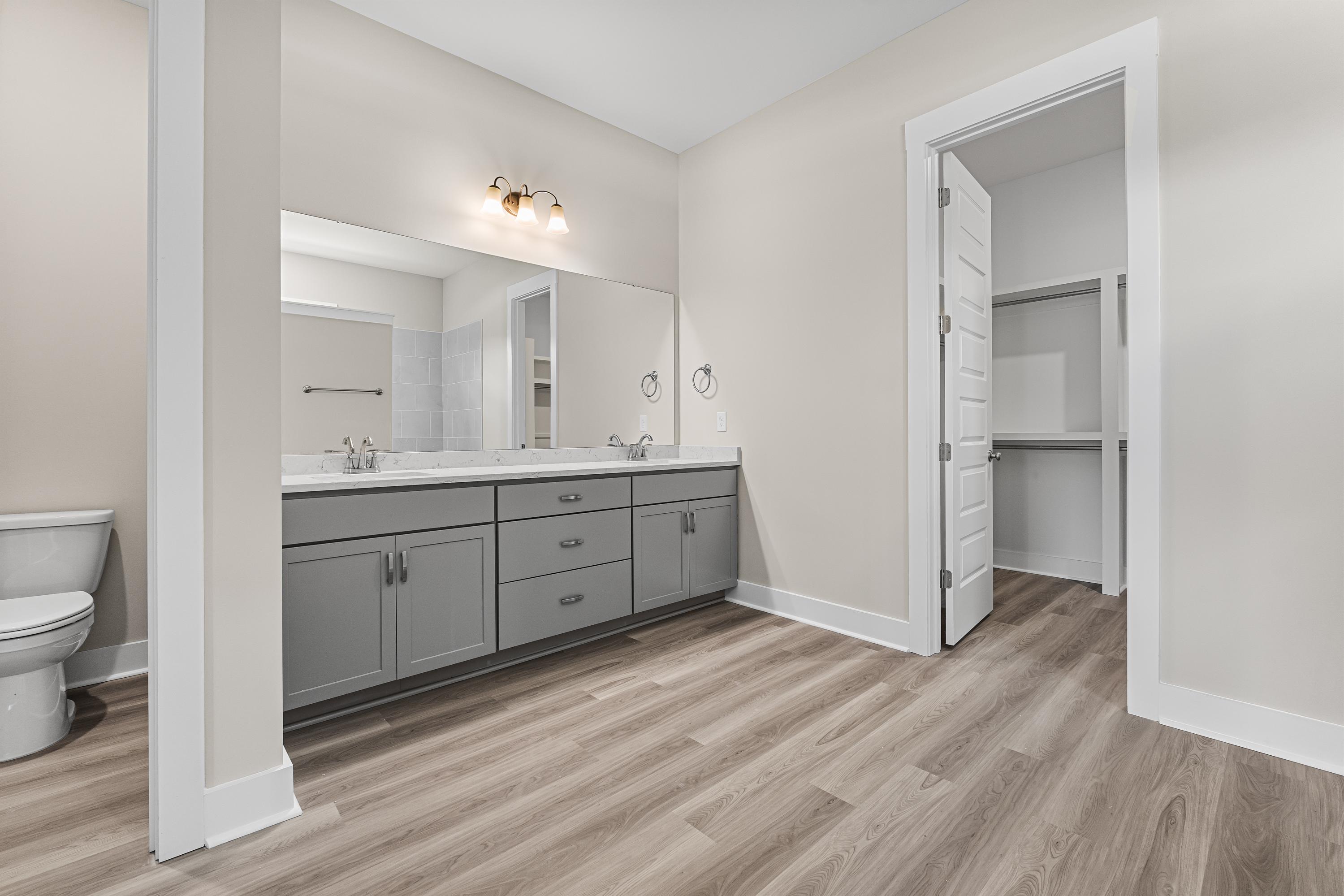 Spacious master bathroom in The Oxford A featuring double gray vanity, beige walls, wood flooring, and walk-in closet