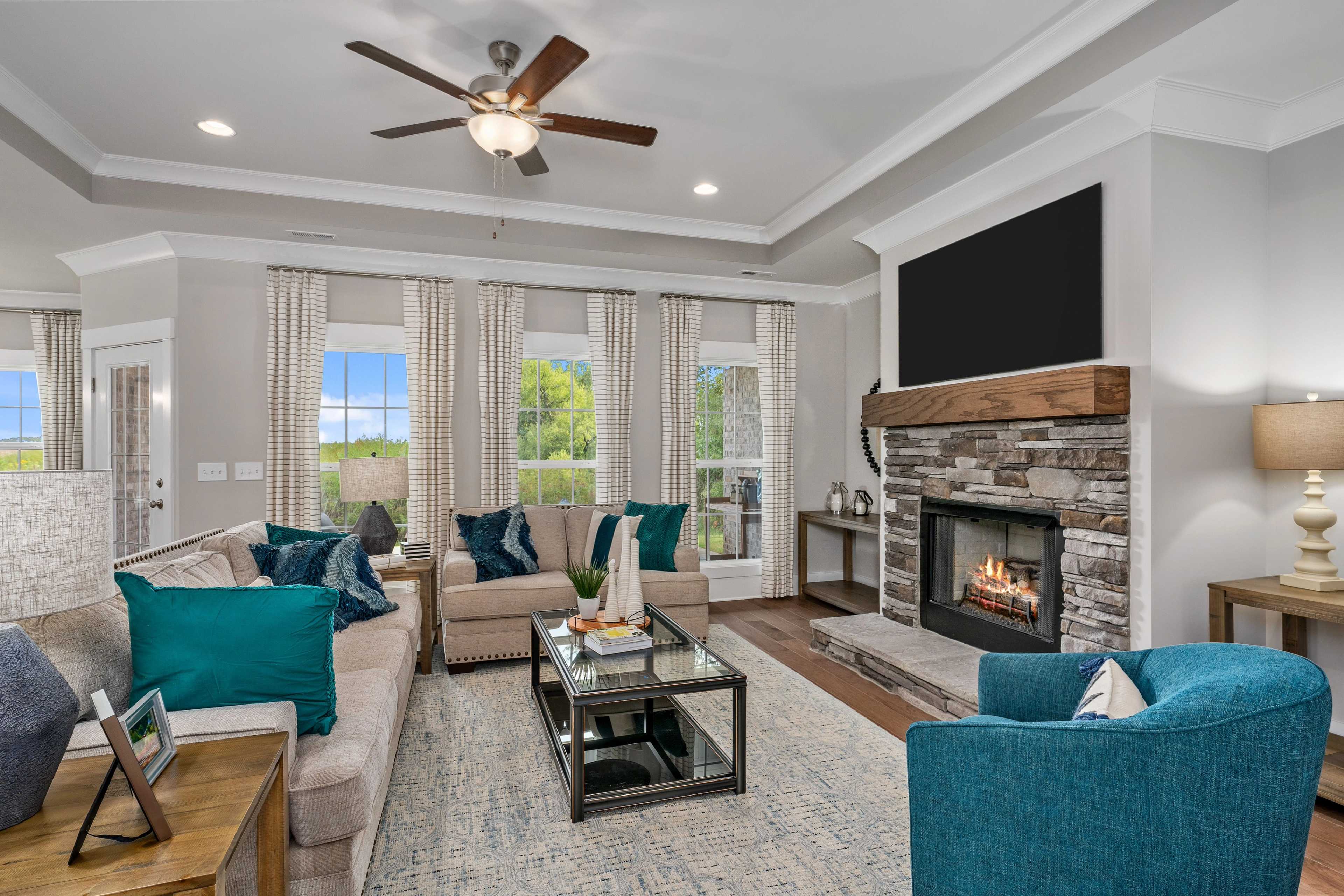 Cozy living room at Kendall Downs in Toney Alabama with stone fireplace, sectional sofa, large windows, and hardwood floors