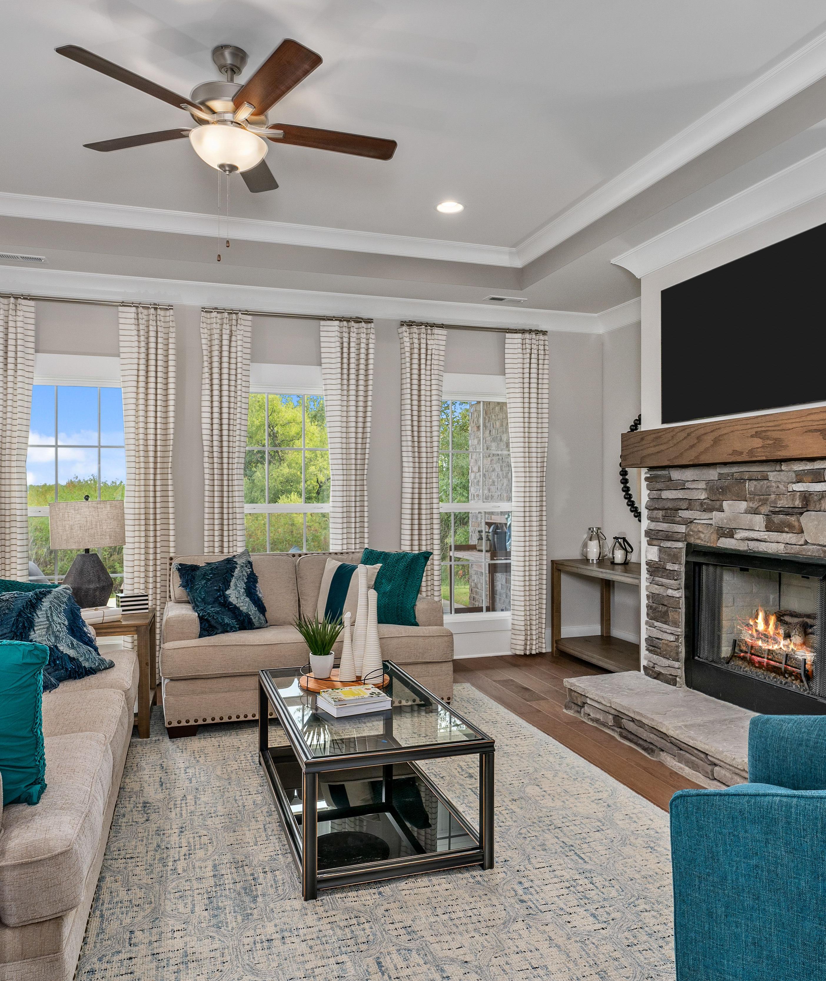 Cozy living room at Kendall Downs in Toney Alabama with stone fireplace, sectional sofa, large windows, and hardwood floors