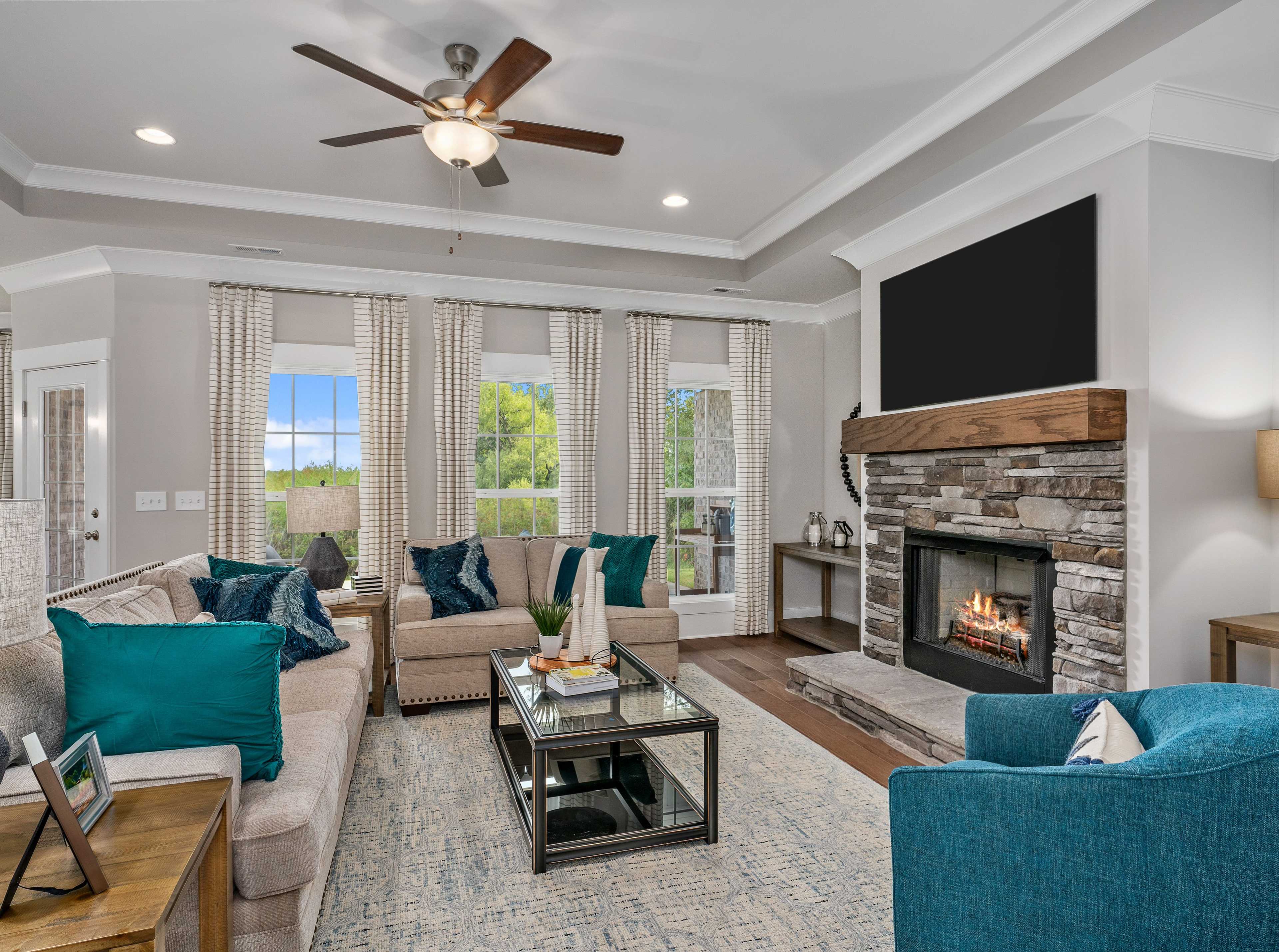 Cozy living room at Kendall Downs in Toney Alabama with stone fireplace, sectional sofa, large windows, and hardwood floors