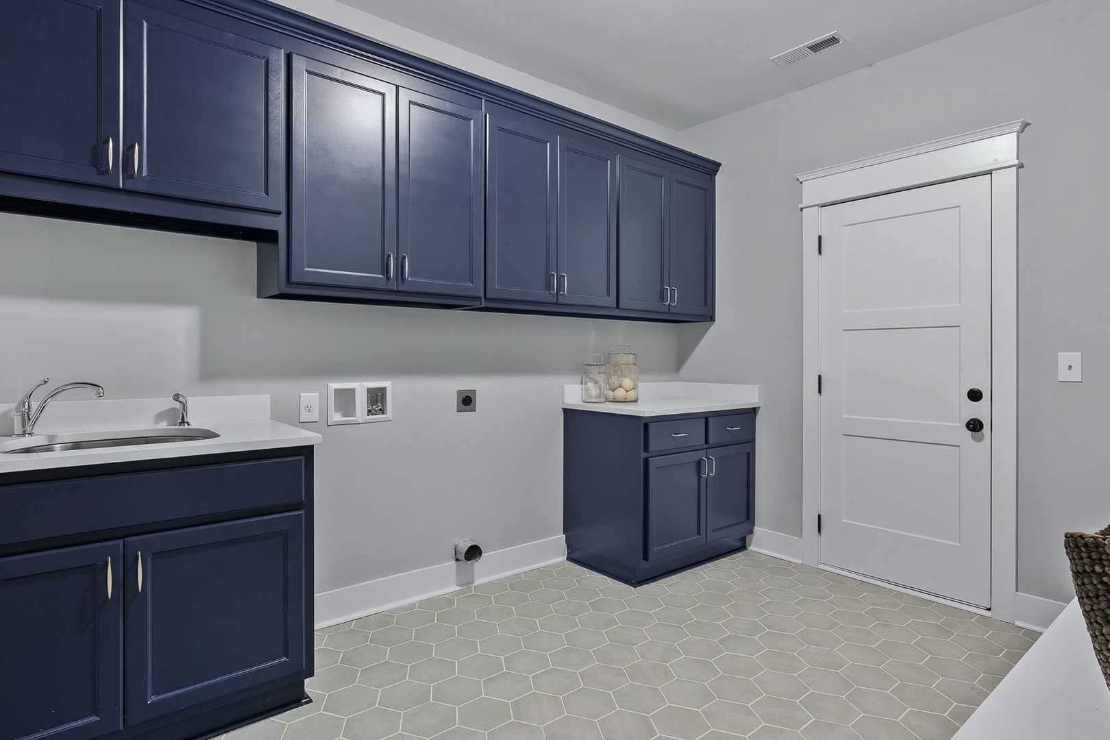 Spacious laundry room in The Oxford with navy blue cabinets, white countertop sink, and hex tile floor