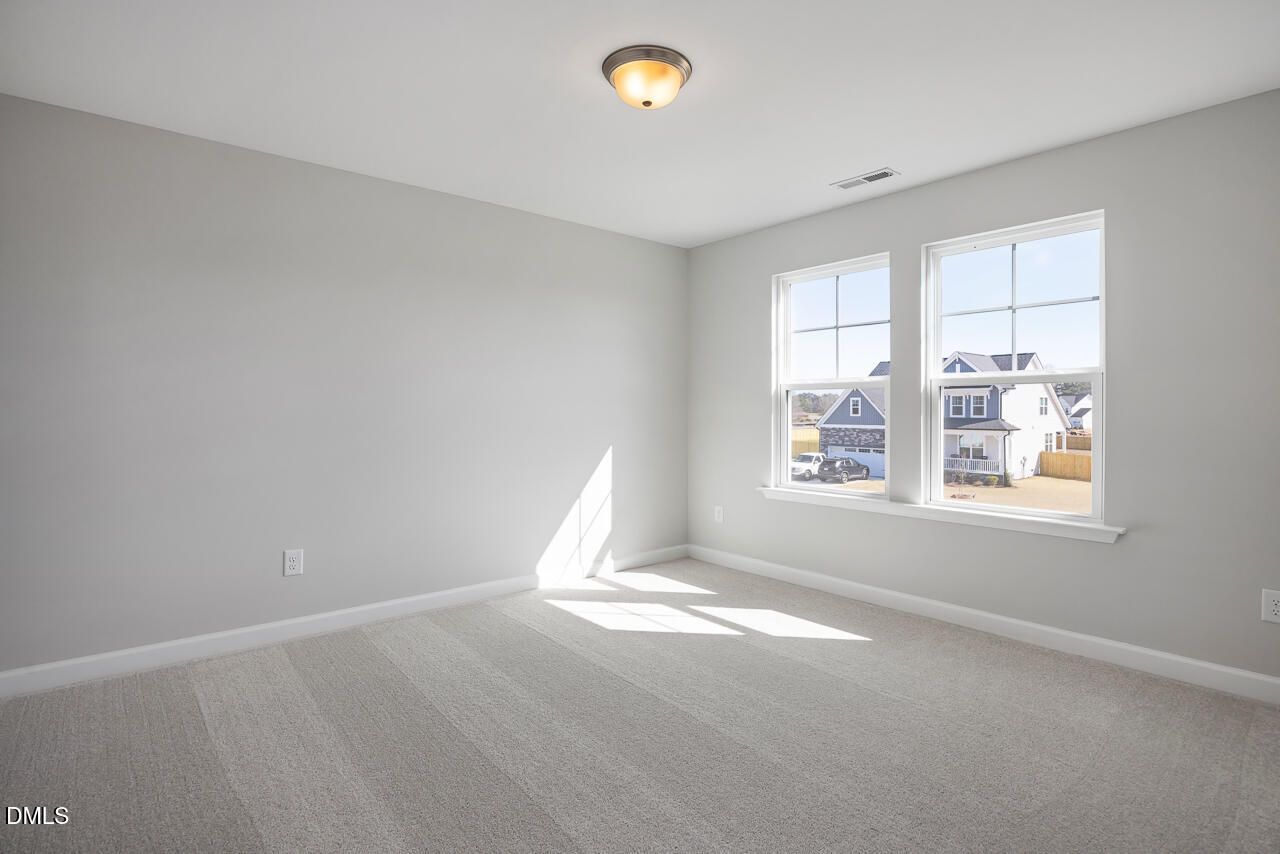 Bright secondary bedroom with gray walls, carpet, flush mount light, and large windows showing neighborhood view in The Willow G, Angier, NC