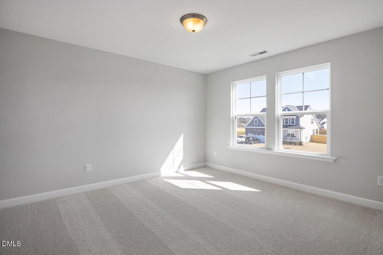 Bright secondary bedroom with gray walls, carpet, flush mount light, and large windows showing neighborhood view in The Willow G, Angier, NC
