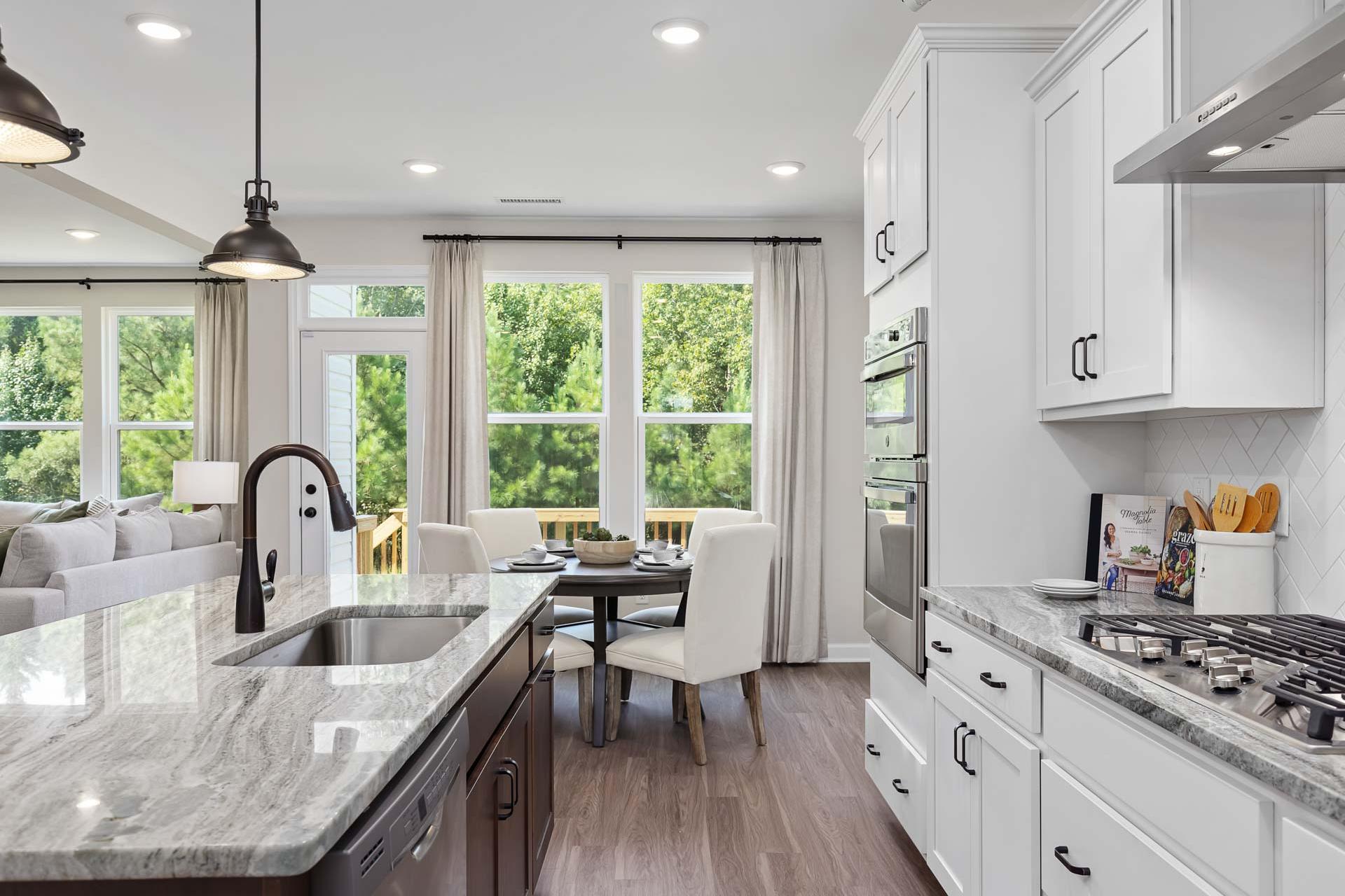 Open-concept kitchen and dining area at Sierra Heights in Clayton NC with white shaker cabinets, granite island, stainless appliances, and hardwood floors