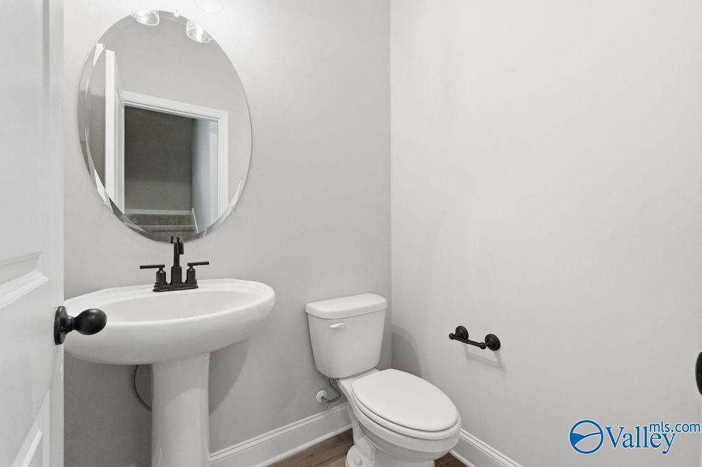 Modern half-bath with pedestal sink, oval mirror, and matte black fixtures in The Rockford floor plan, Hartselle, AL.