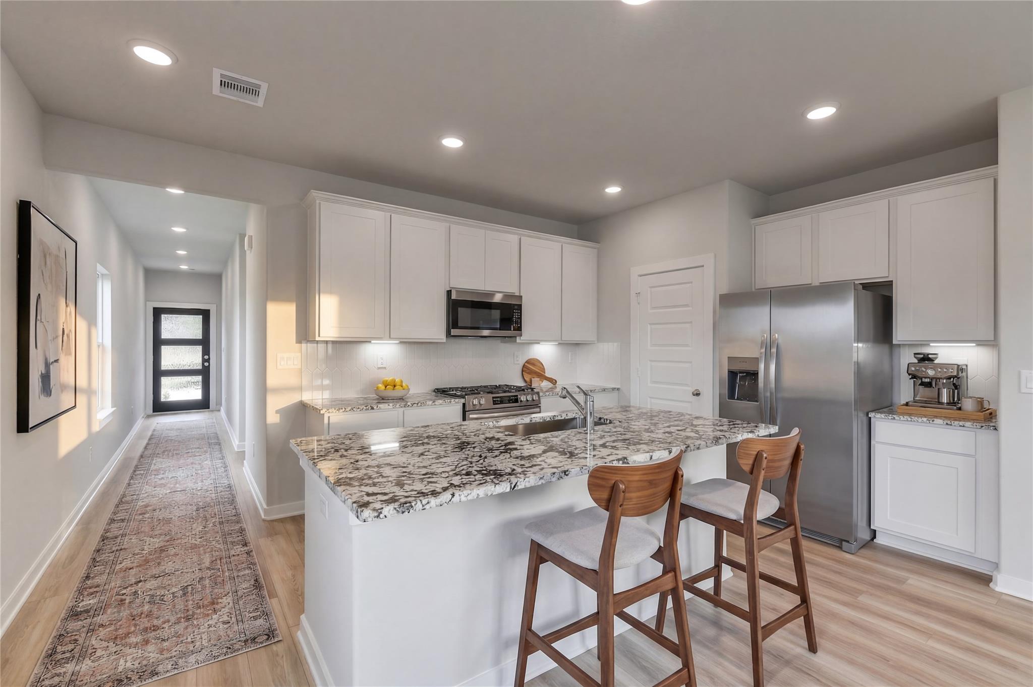 Modern kitchen with granite island and white cabinets in The Colorado G floor plan at Windmill Estates, Magnolia, Texas.