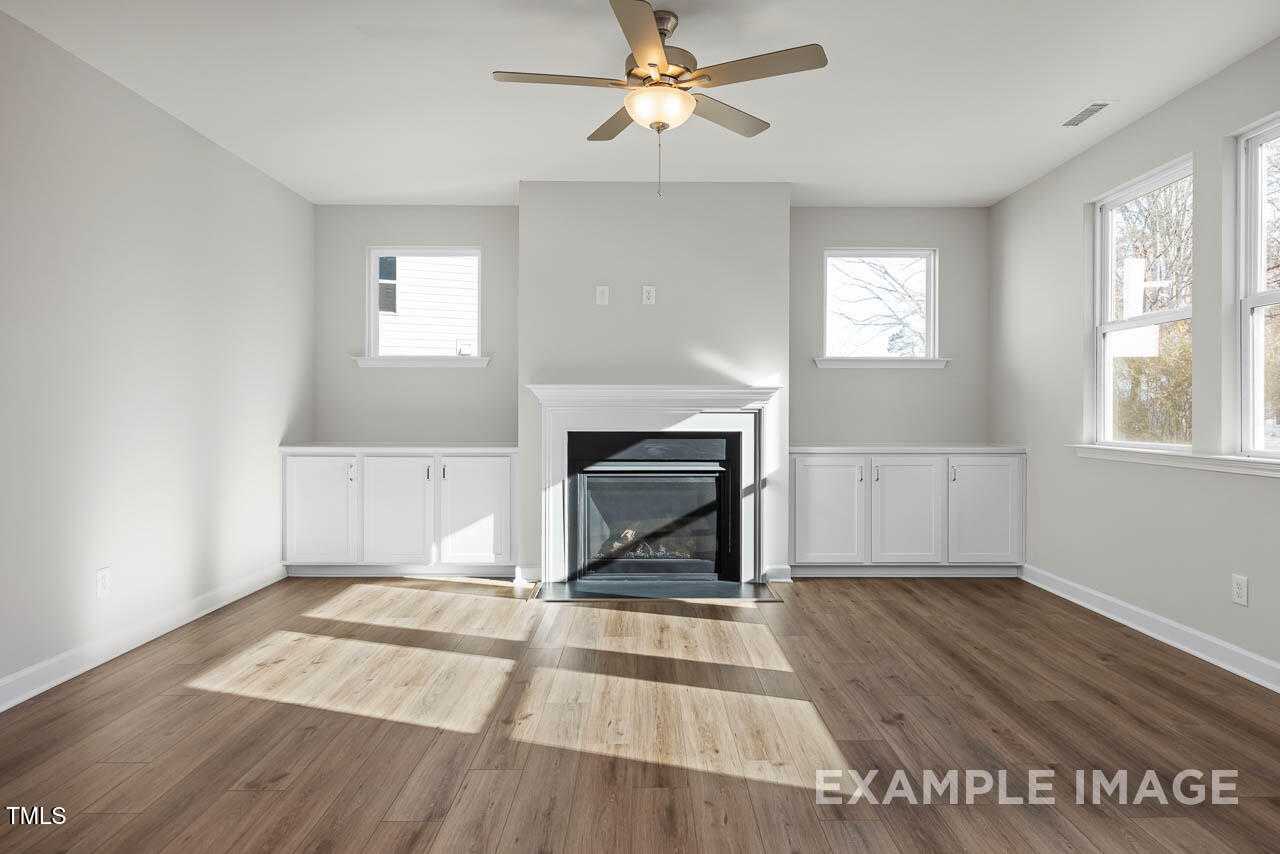 Cozy family room with gas fireplace, white built-in cabinets, hardwood floors, ceiling fan, and large windows in Davidson Homes The Hickory II B, Lillington, NC