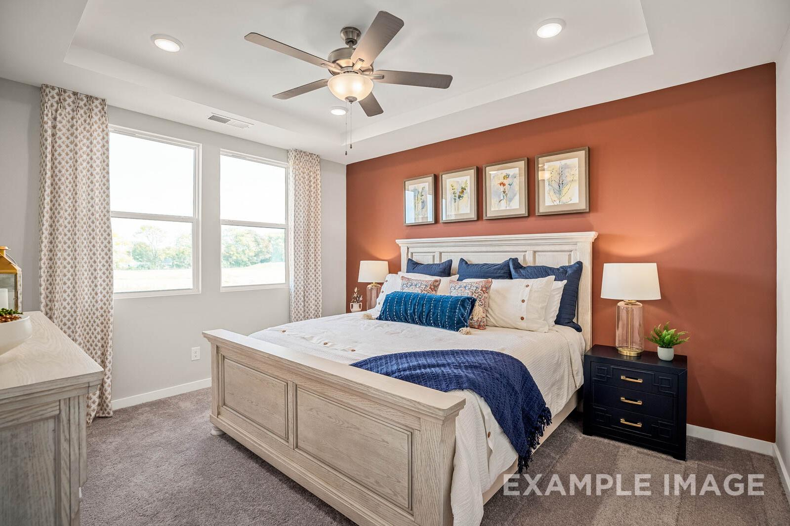 Spacious master bedroom in The Franklin B with king bed, navy bedding, orange accent wall, and large curtained windows