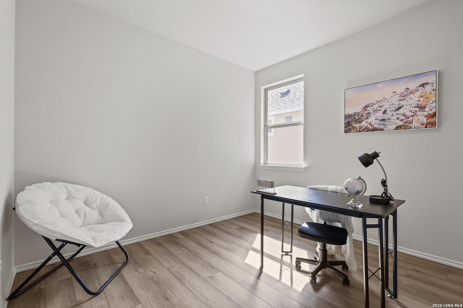 Cozy home office with black metal desk, ergonomic chair, white pouf seating, and window art in The Daphne H, Seguin, Texas