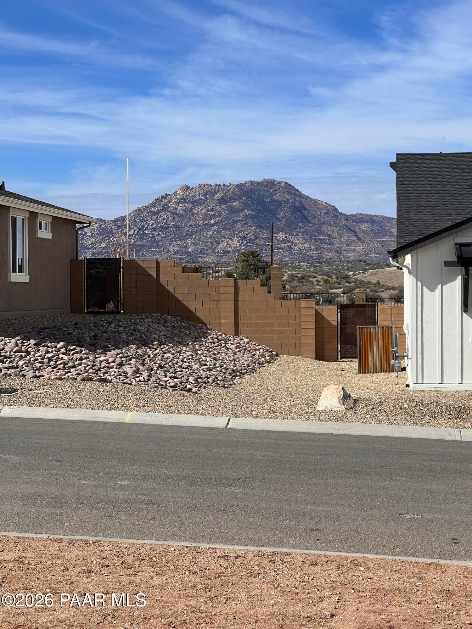 Modern 1-story home exterior with beige stucco, stone walls, wooden gate, and mountain view in Westwood, Prescott, Arizona