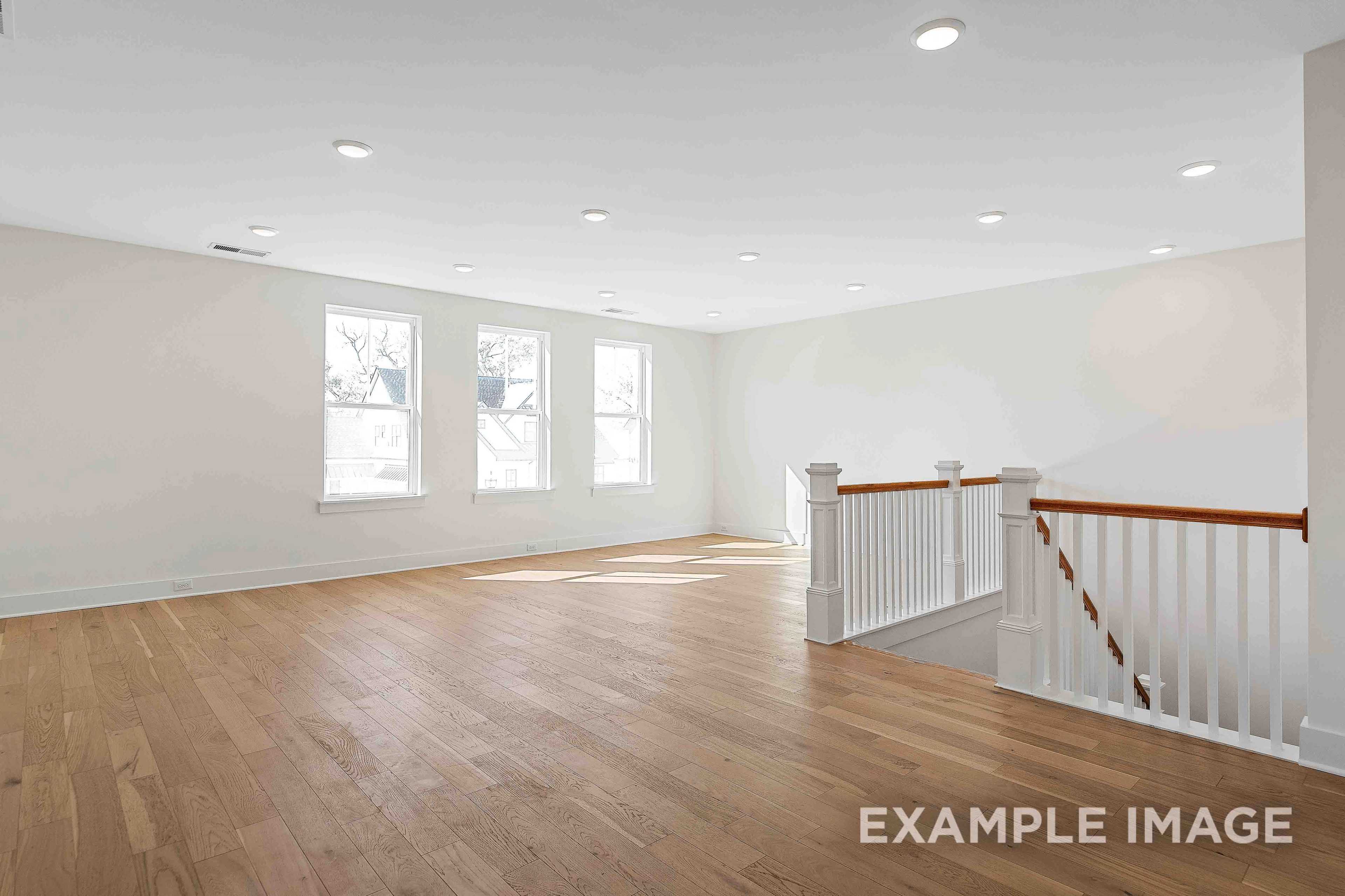 Spacious upper floor loft in The Albany A featuring hardwood floors, large windows, and wooden balustrade staircase