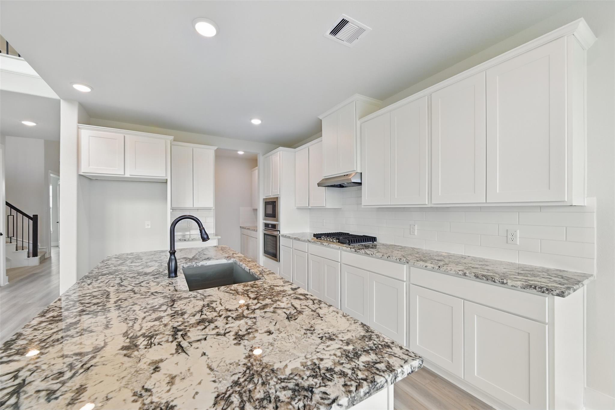 Modern kitchen with white shaker cabinets, speckled granite island sink, stainless steel appliances in Davidson Homes The Victoria C, Lago Mar