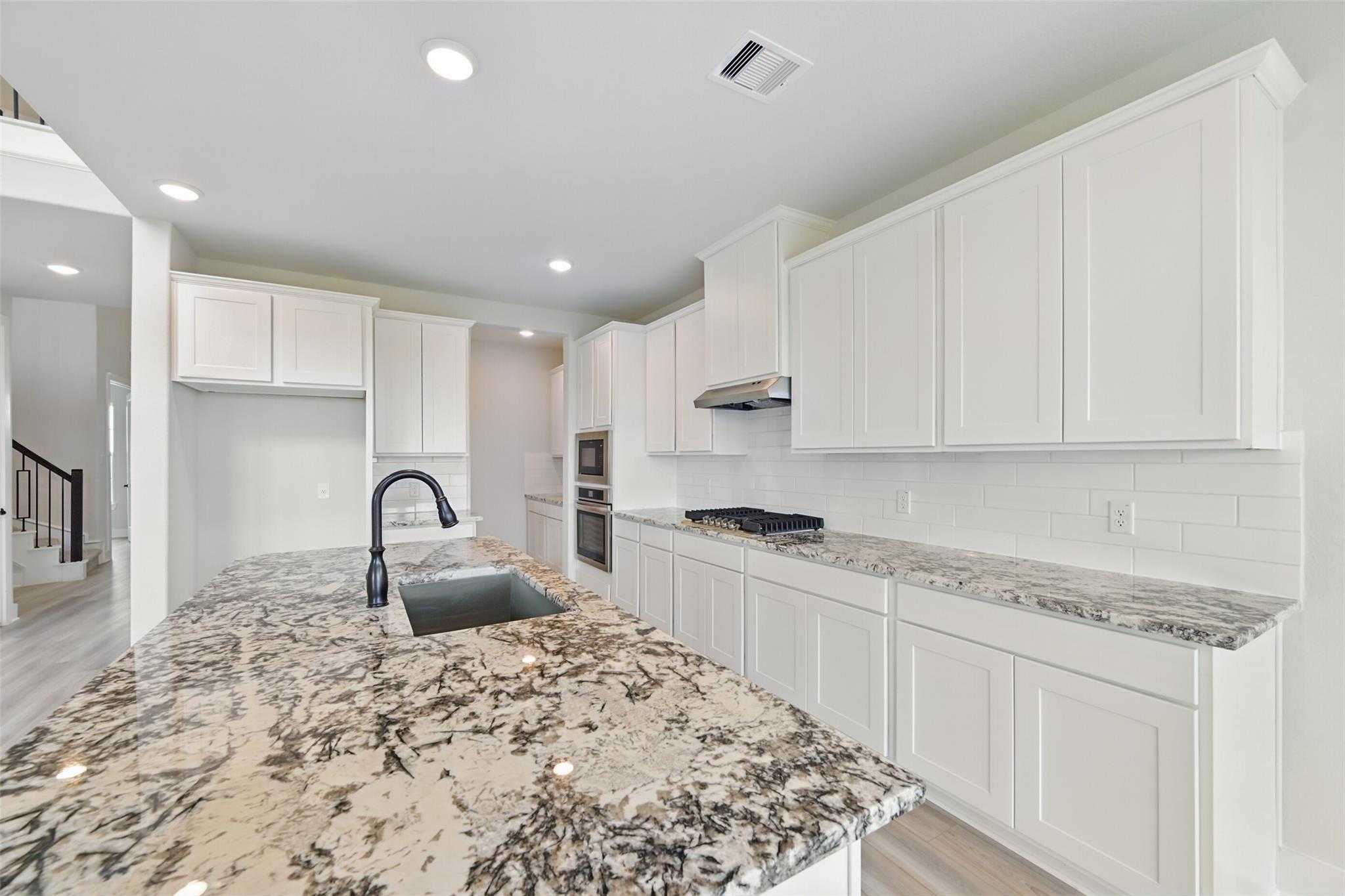 Modern white kitchen with granite island, undermount sink, stainless double oven in Davidson Homes The Victoria C, Lago Mar, Texas City