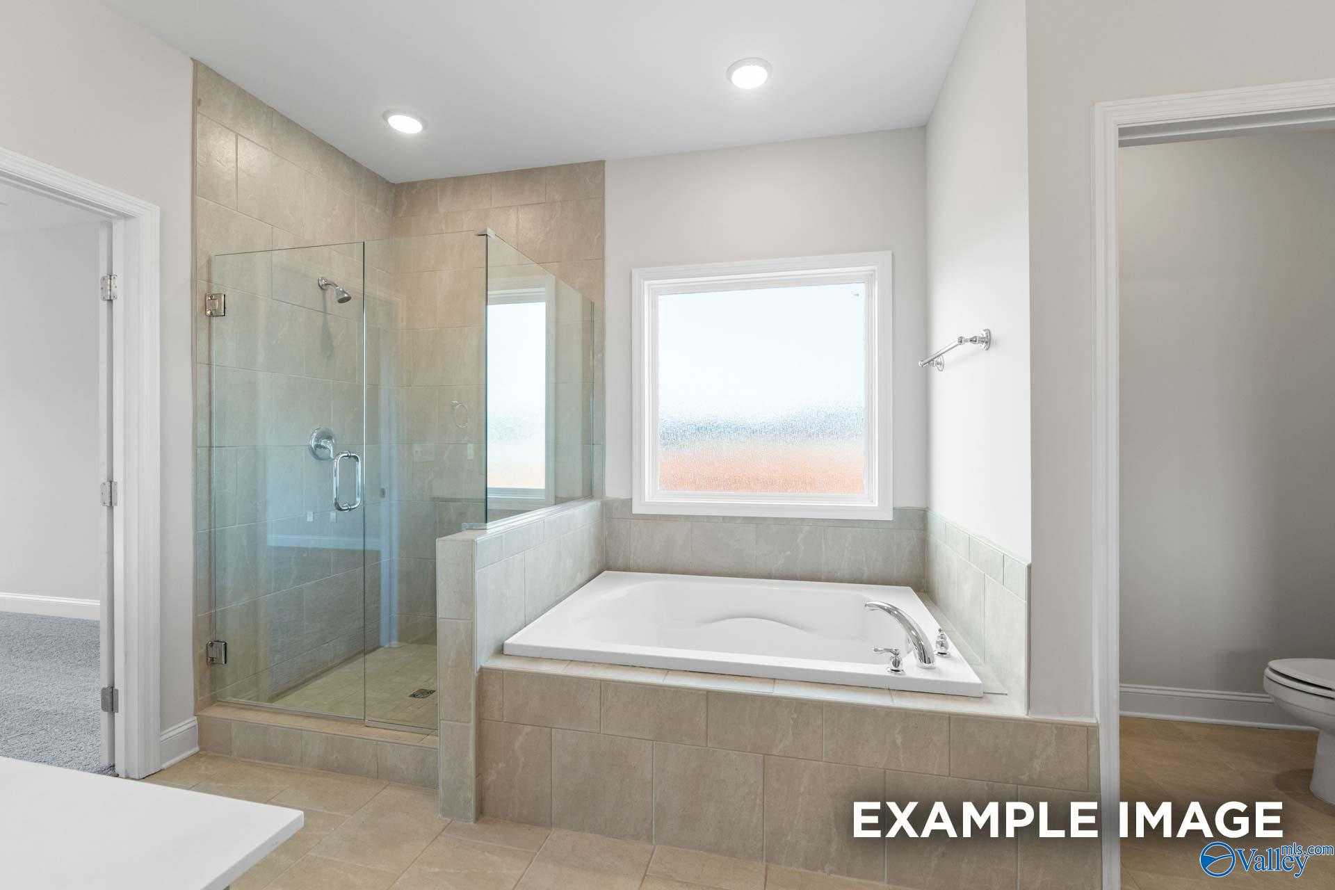 Elegant master bathroom featuring glass walk-in shower, soaking tub, and large window in Davidson Homes The Lanier, Toney, Alabama