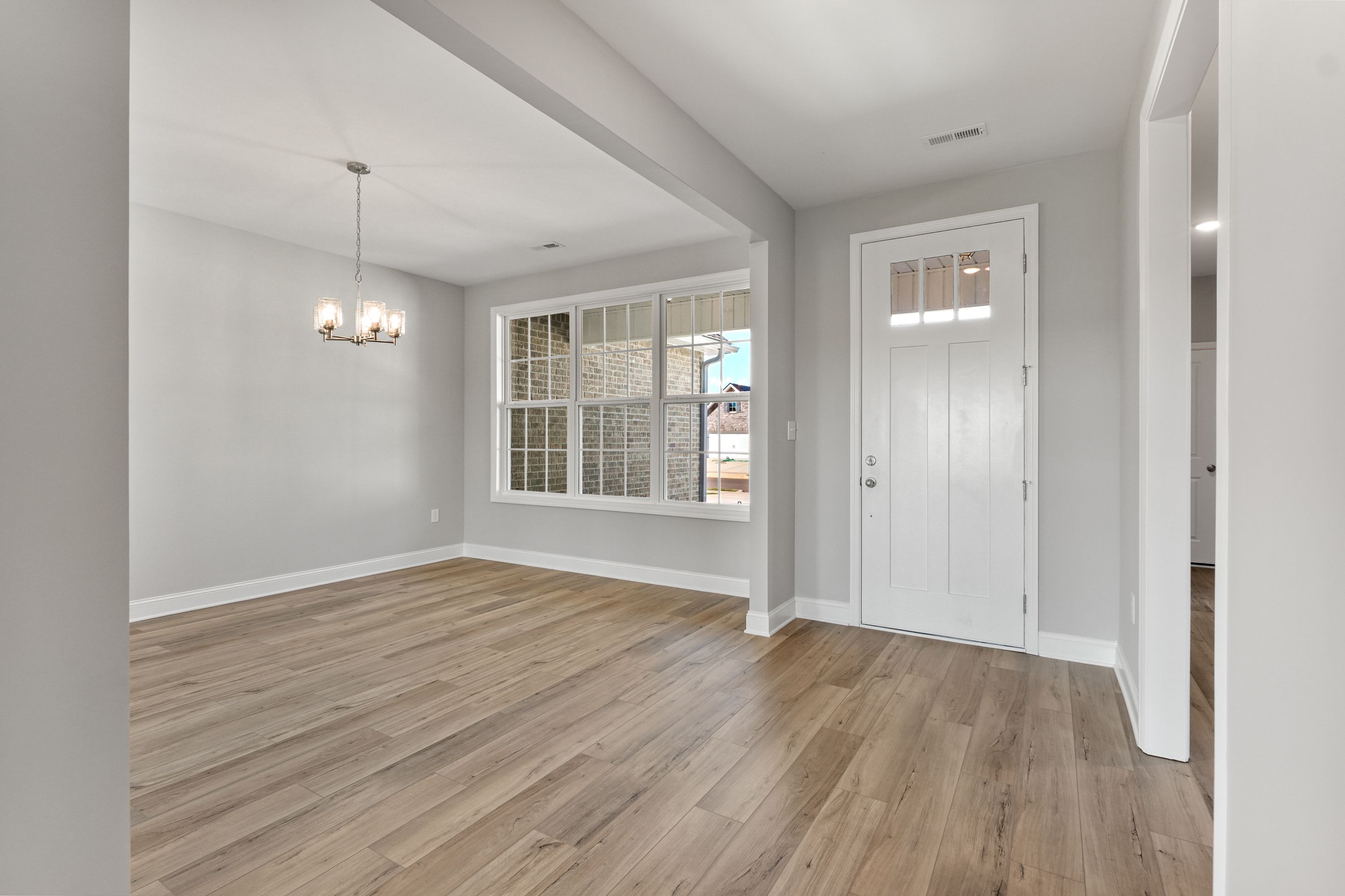Spacious entryway in The Valencia home design by Davidson Homes featuring light gray walls, oak hardwood floors, chandelier, and large window view