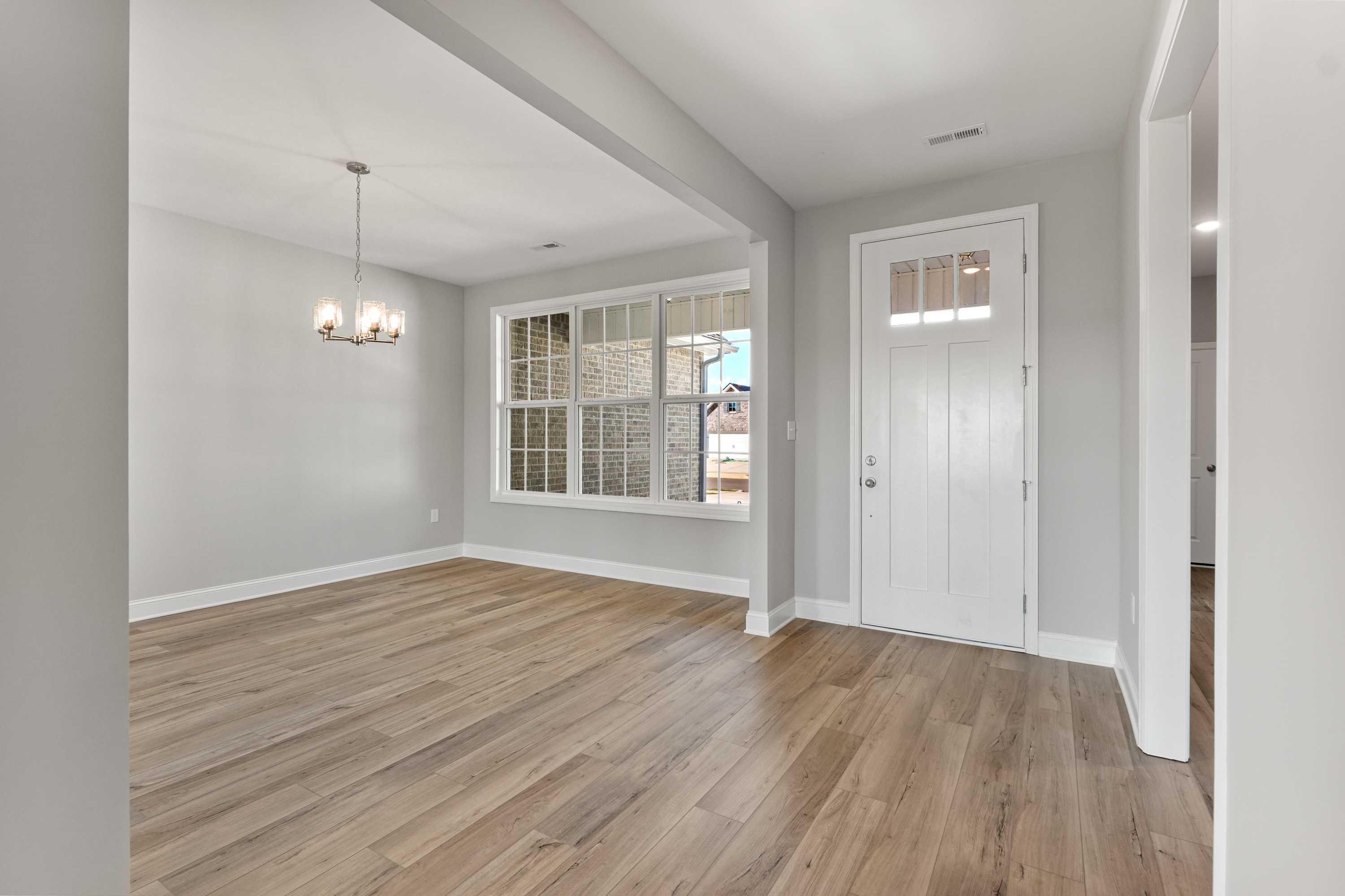 Spacious entryway in The Valencia home design by Davidson Homes featuring light gray walls, oak hardwood floors, chandelier, and large window view