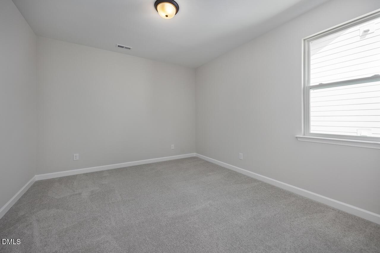 Bright, carpeted secondary bedroom with neutral walls in The Ashport L floor plan at Sage on North Main, Wake Forest, NC.