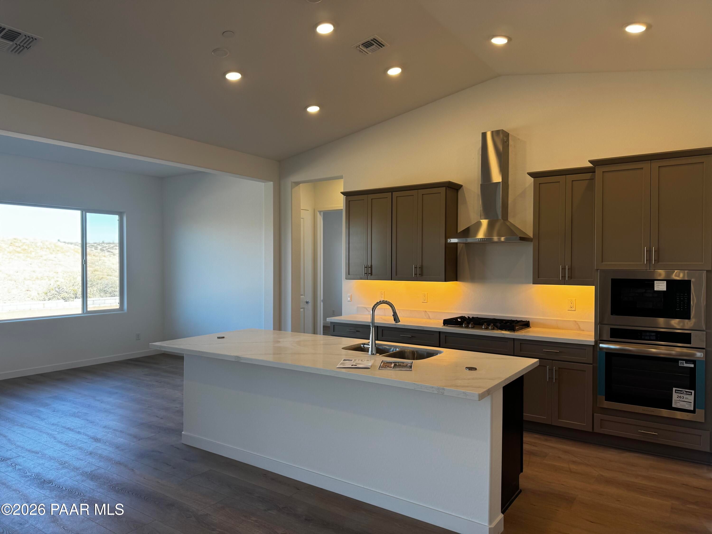 Modern kitchen with white island, gas cooktop, stainless oven, dark cabinets, and desert-view window in Prescott Arizona home