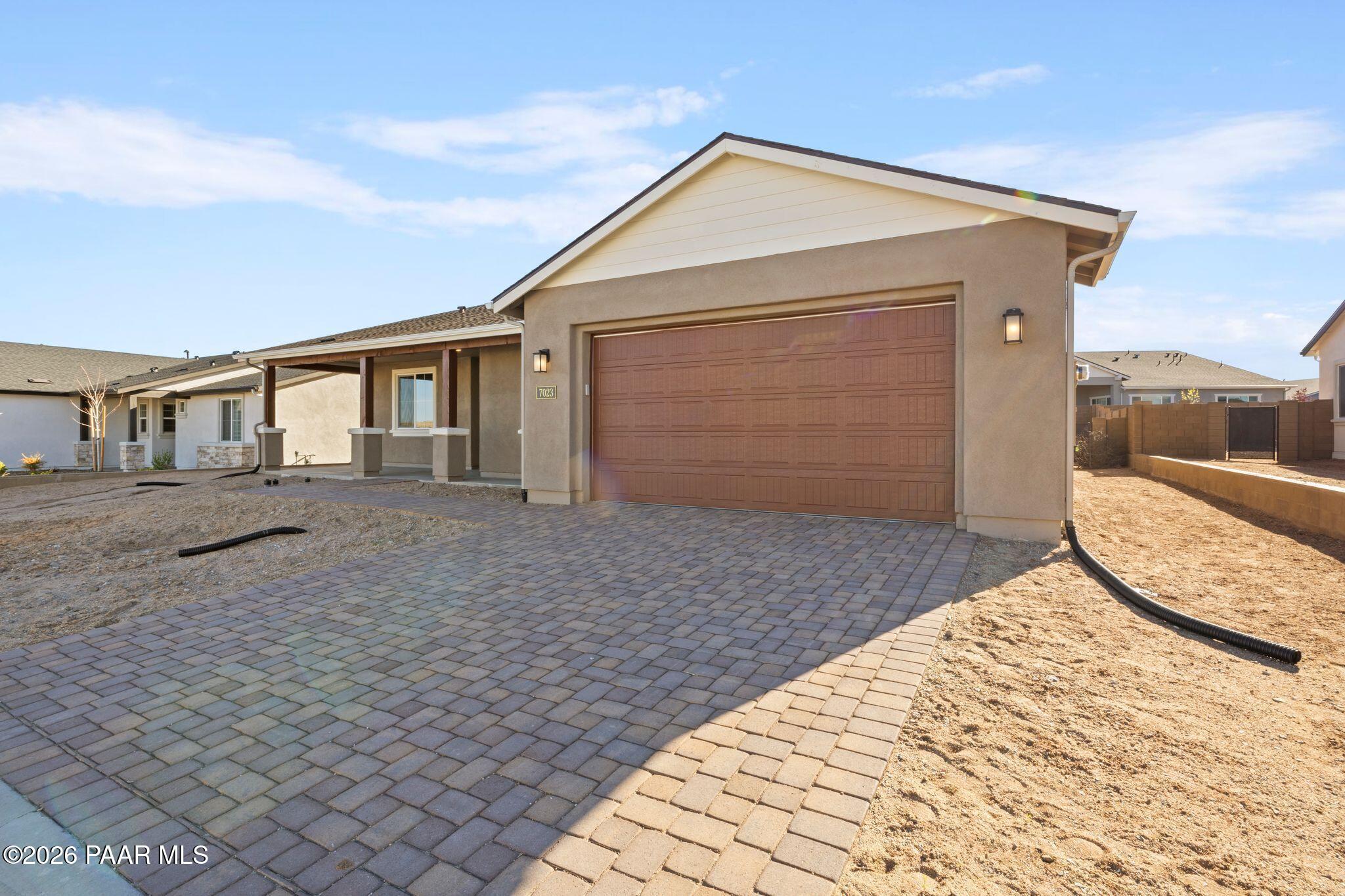 Modern 1-story beige stucco home with open 3-car garage and paver driveway in Westwood, Prescott, Arizona - Davidson Homes Sunrise II A