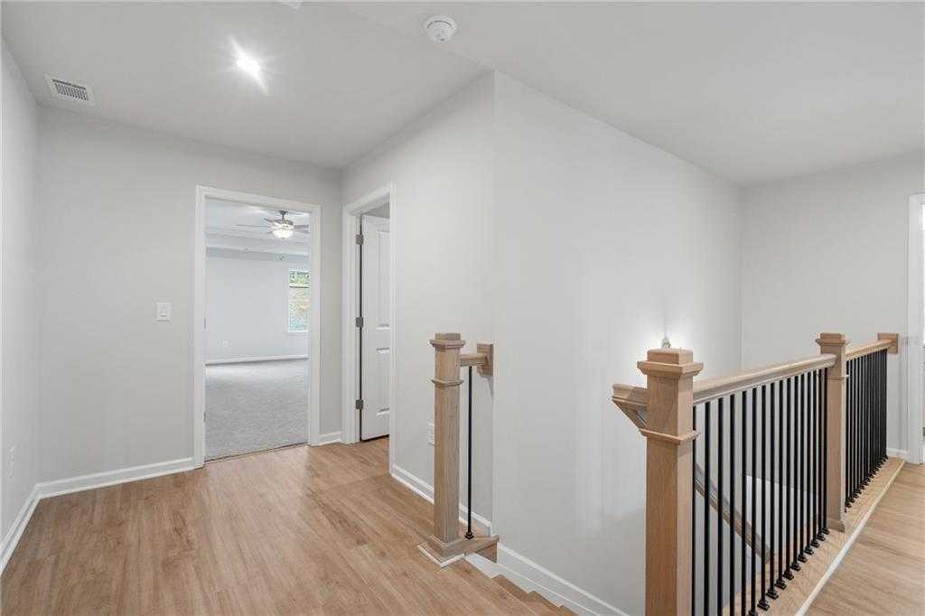Spacious upstairs hallway with hardwood floors, white walls, and elegant oak staircase in Davidson Homes The Cary A, Kennesaw, Georgia