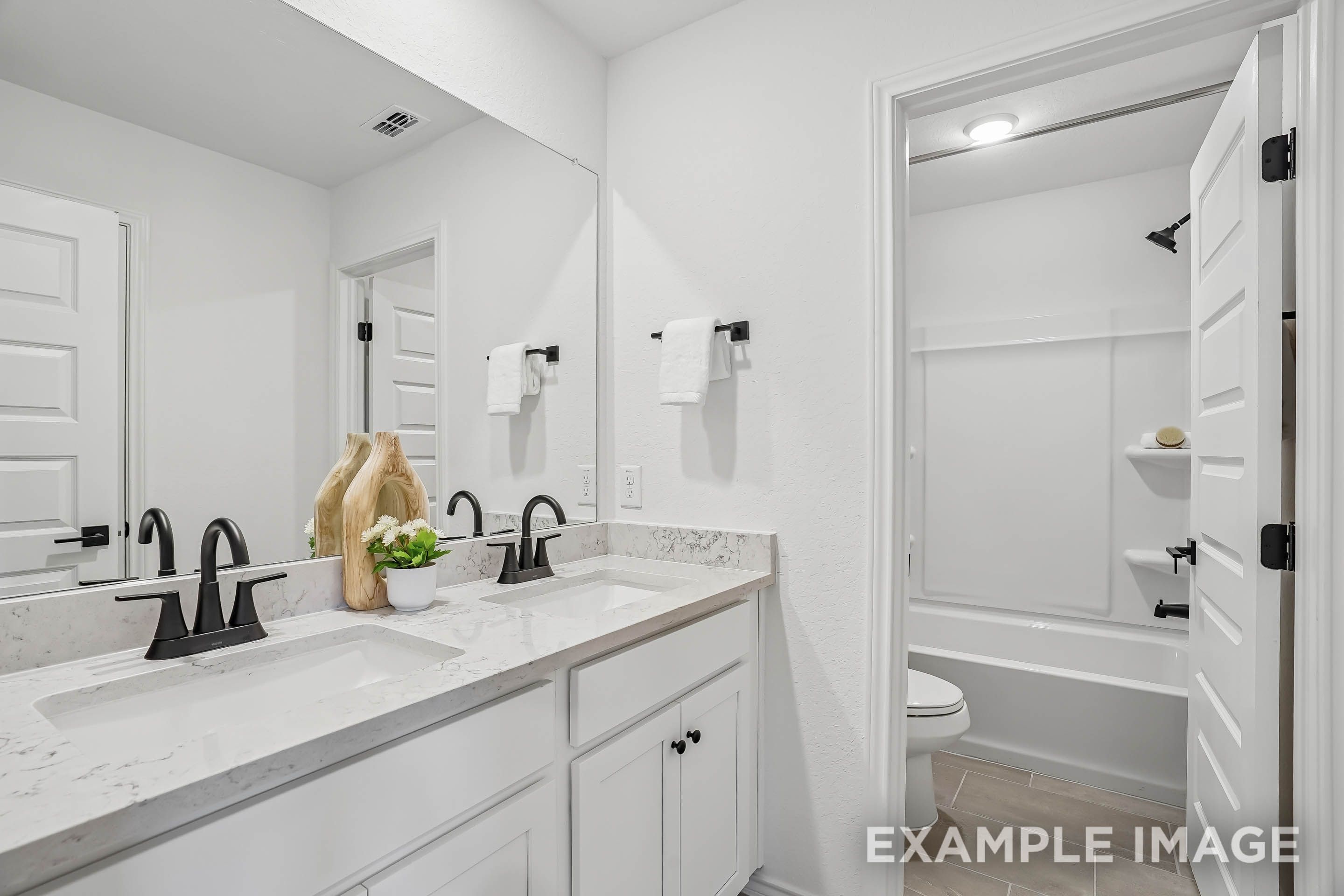 Modern bathroom in The Pinecrest D featuring a dual-sink vanity, marble countertops, and black fixtures.