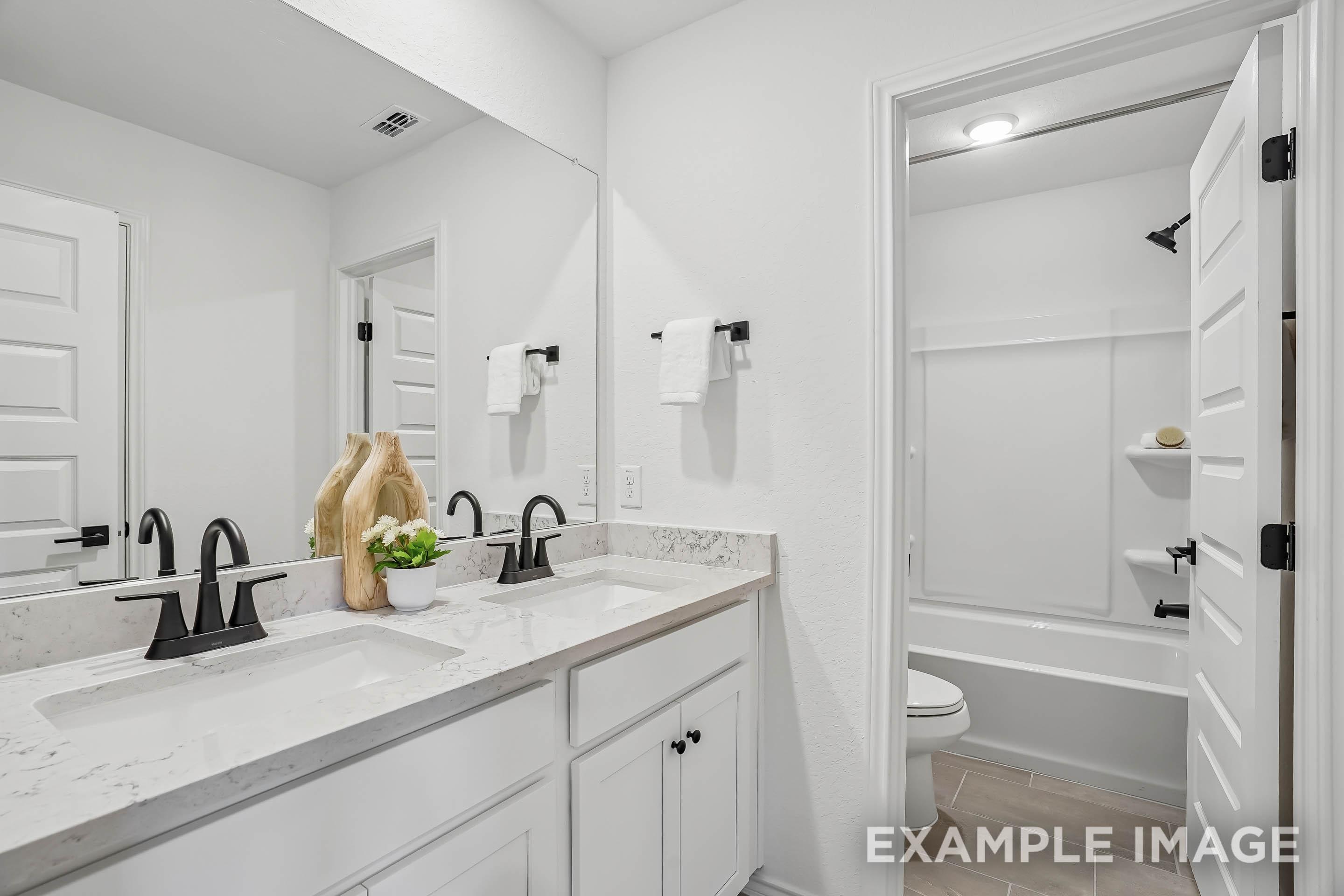 Modern bathroom in The Pinecrest D featuring a dual-sink vanity, marble countertops, and black fixtures.