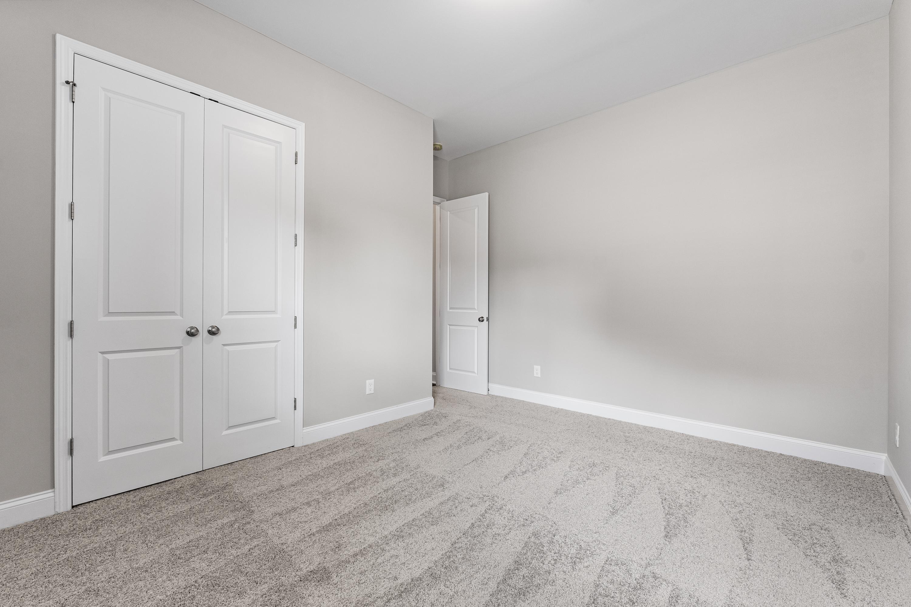 Spacious Arcadia B bedroom interior with white double closet doors, light gray walls, and neutral carpet floor