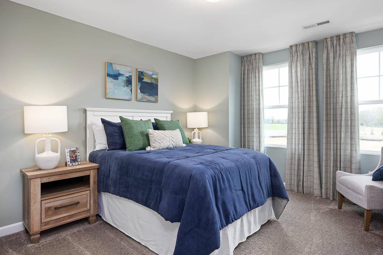 Spacious bedroom at Gregory Village Townhomes in Lillington NC with navy blue bedding, large curtained windows, and neutral gray walls