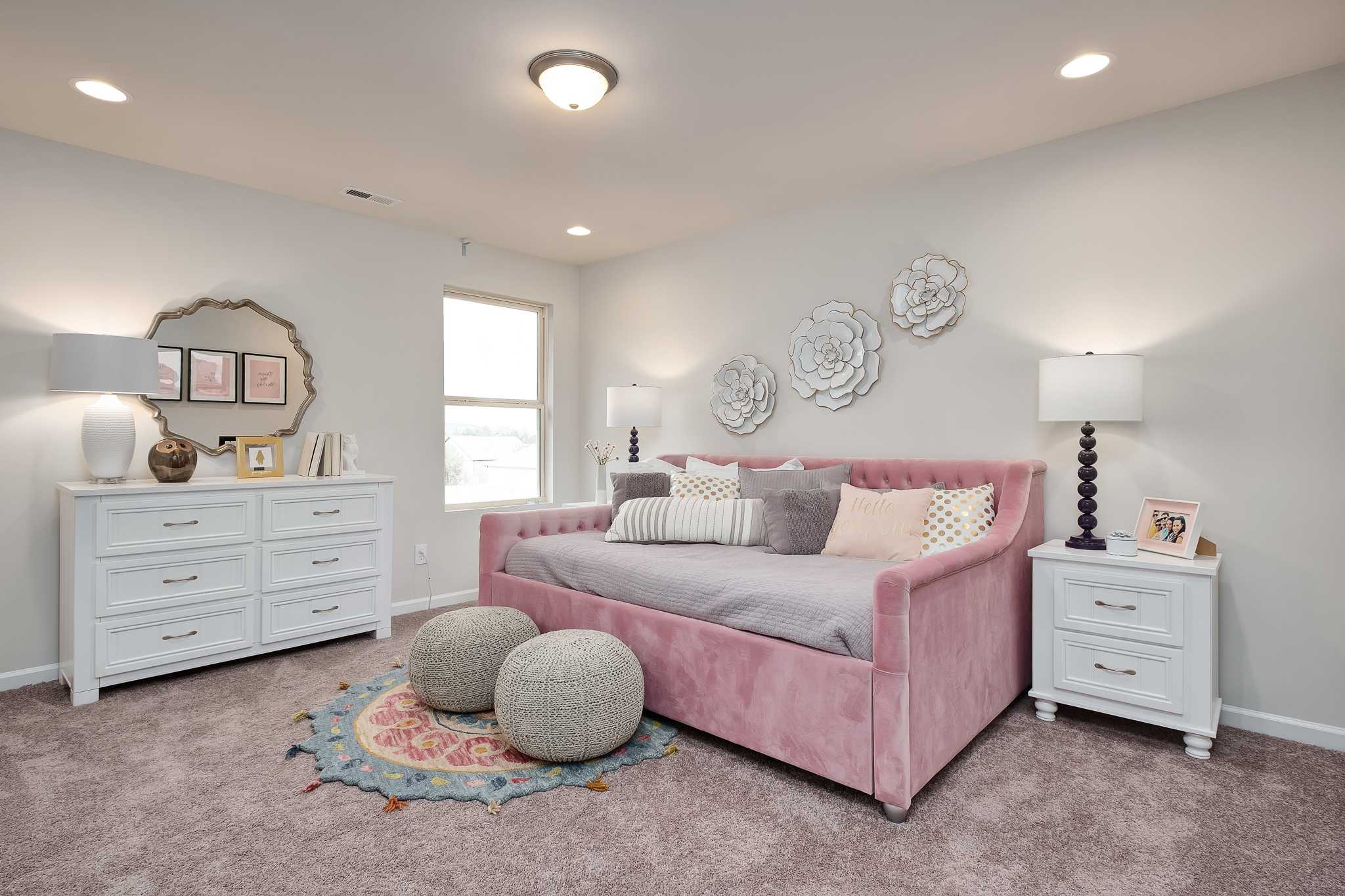 Cozy girl's bedroom with pink trundle bed, white dressers, floral wall art and window at The Reserve at Overton in Hampton Cove, Alabama