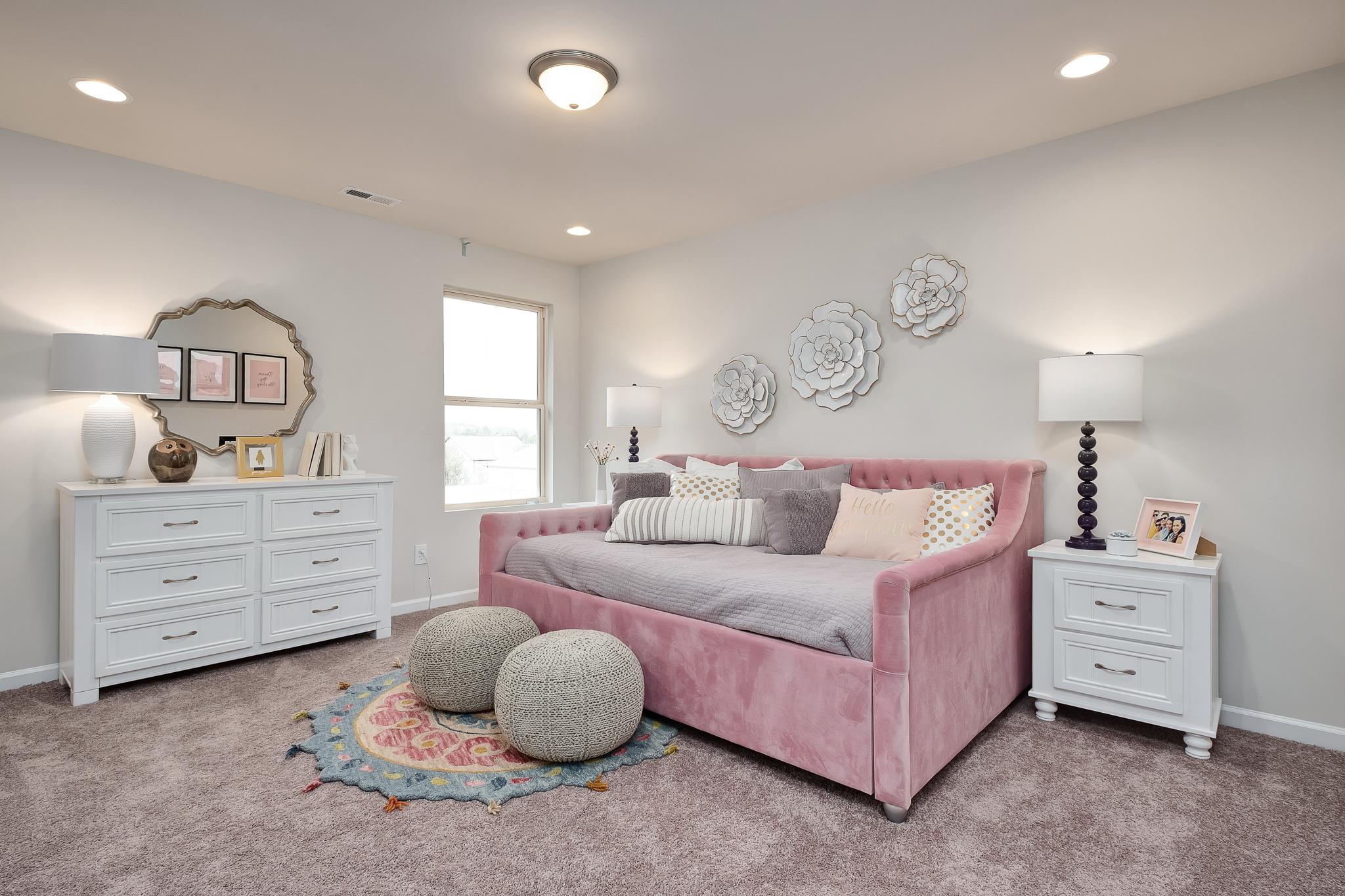 Cozy girl's bedroom with pink trundle bed, white dressers, floral wall art and window at The Reserve at Overton in Hampton Cove, Alabama