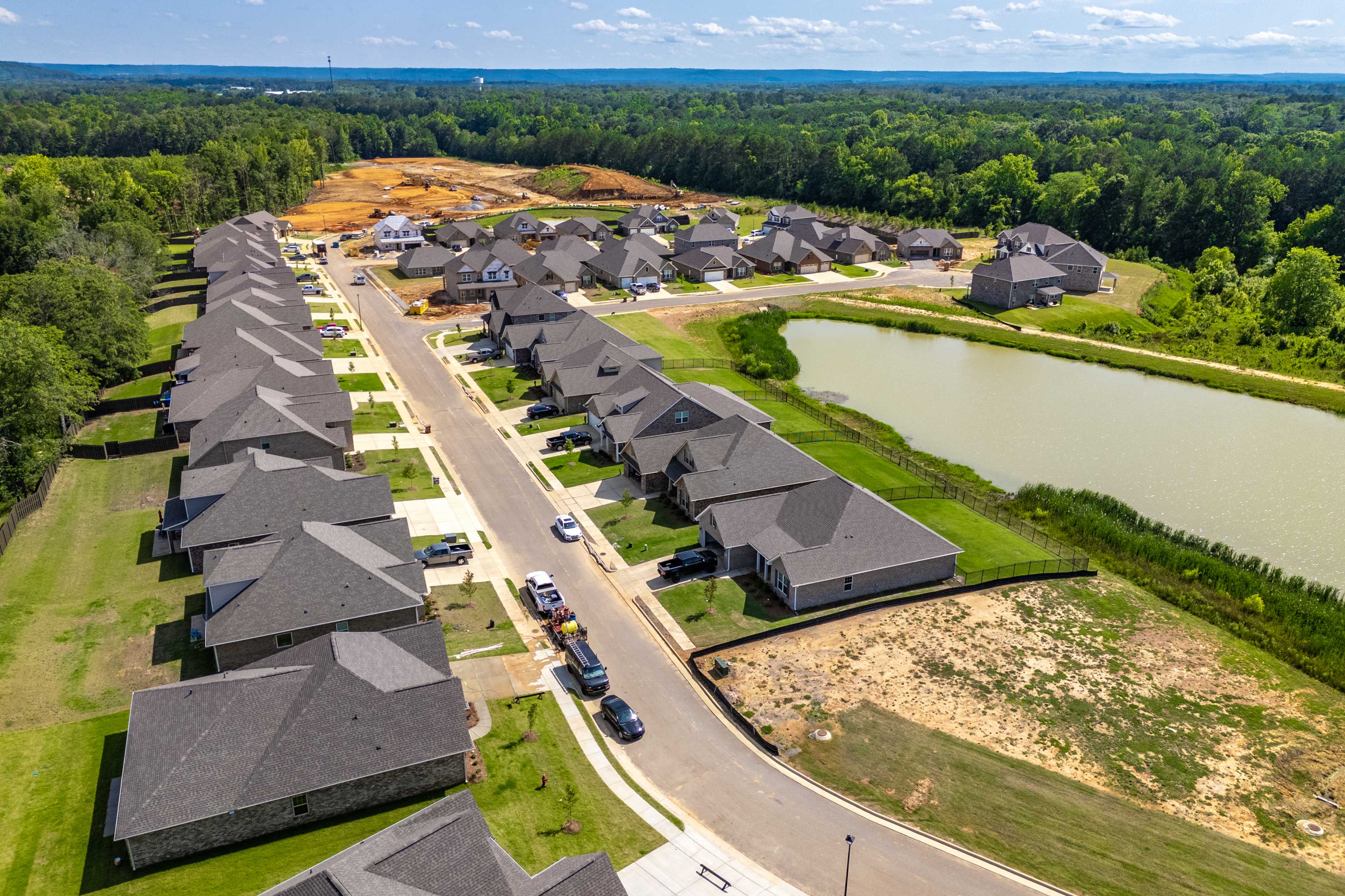 Aerial view of Cain Park neighborhood in Hartselle Alabama with new gray-roofed homes, streets, pond, and green forests