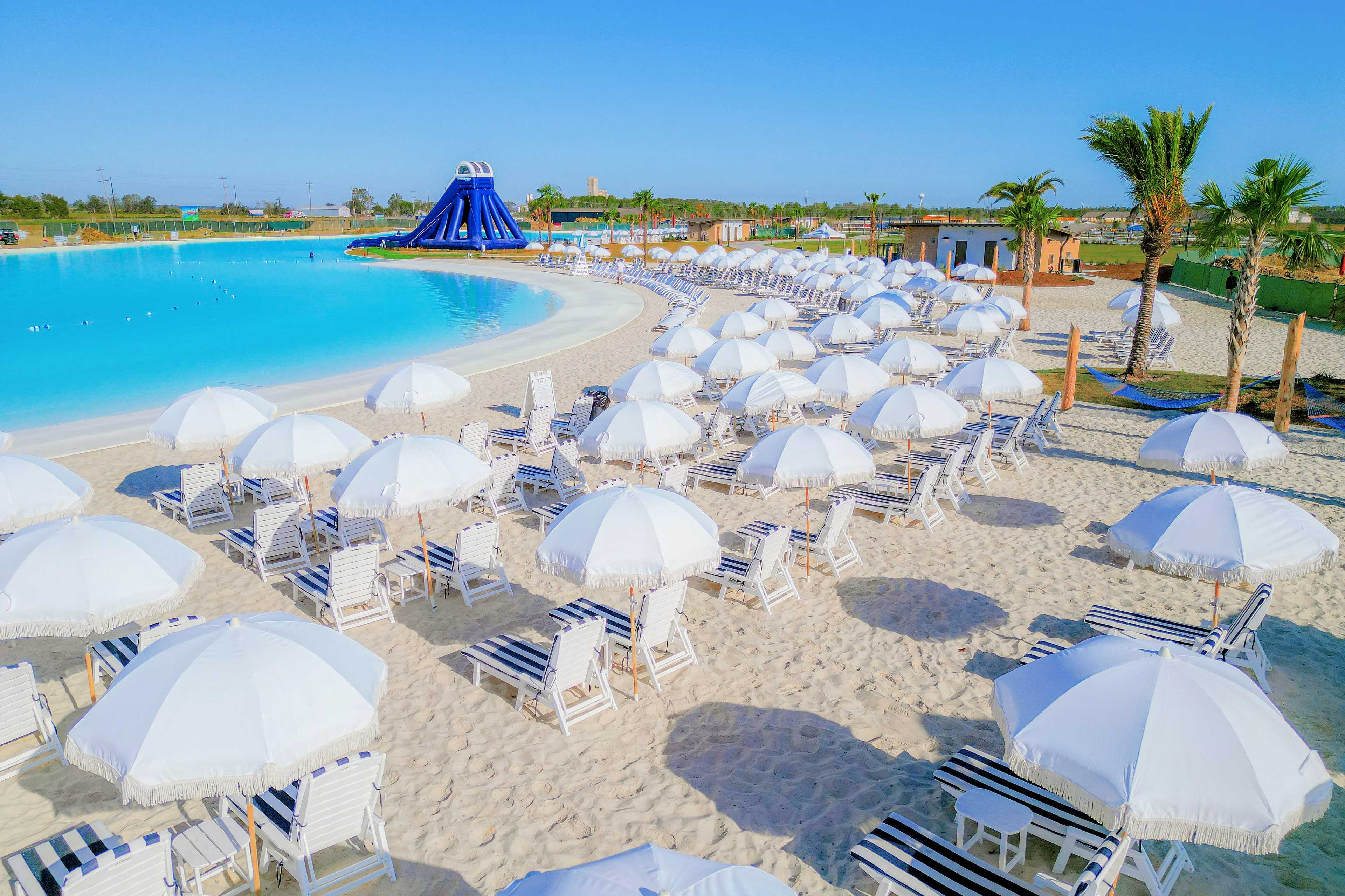 Resort-style lagoon pool at River Ranch Meadows in Dayton Texas with blue waterslide, white umbrellas, and sandy lounge area