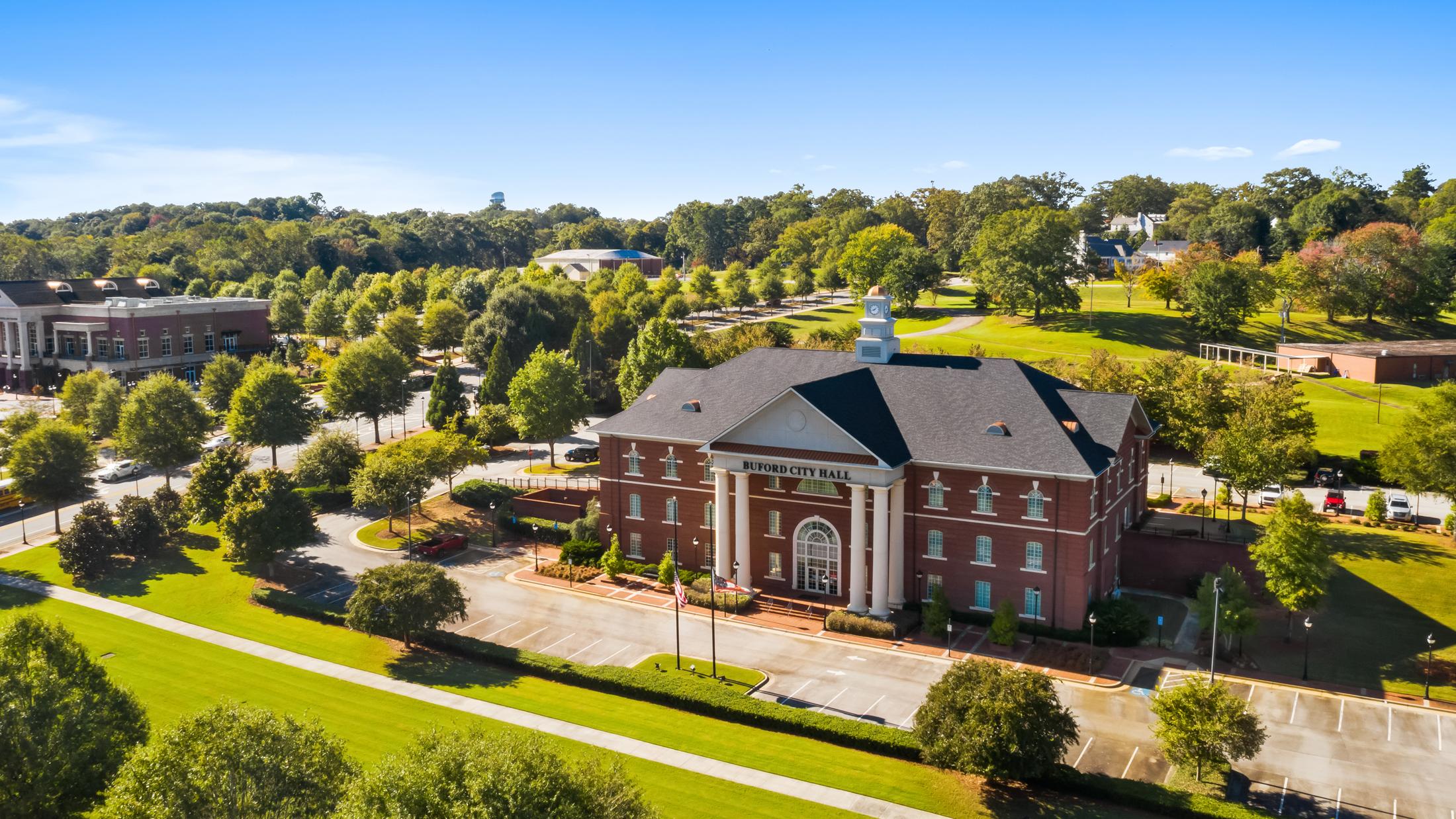 Aerial view of red brick clubhouse with clock tower at The Grove at East Thompson in Buford, Georgia, surrounded by trees and parking