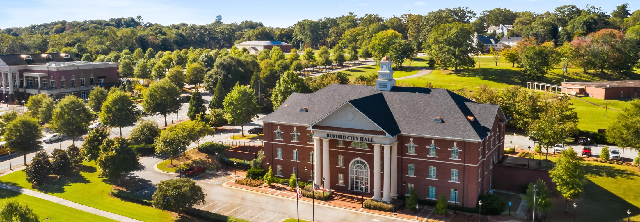 Aerial view of red brick clubhouse with clock tower at The Grove at East Thompson in Buford, Georgia, surrounded by trees and parking