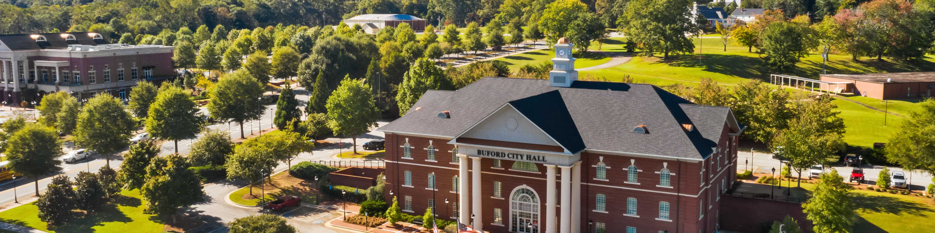 Aerial view of red brick clubhouse with clock tower at The Grove at East Thompson in Buford, Georgia, surrounded by trees and parking