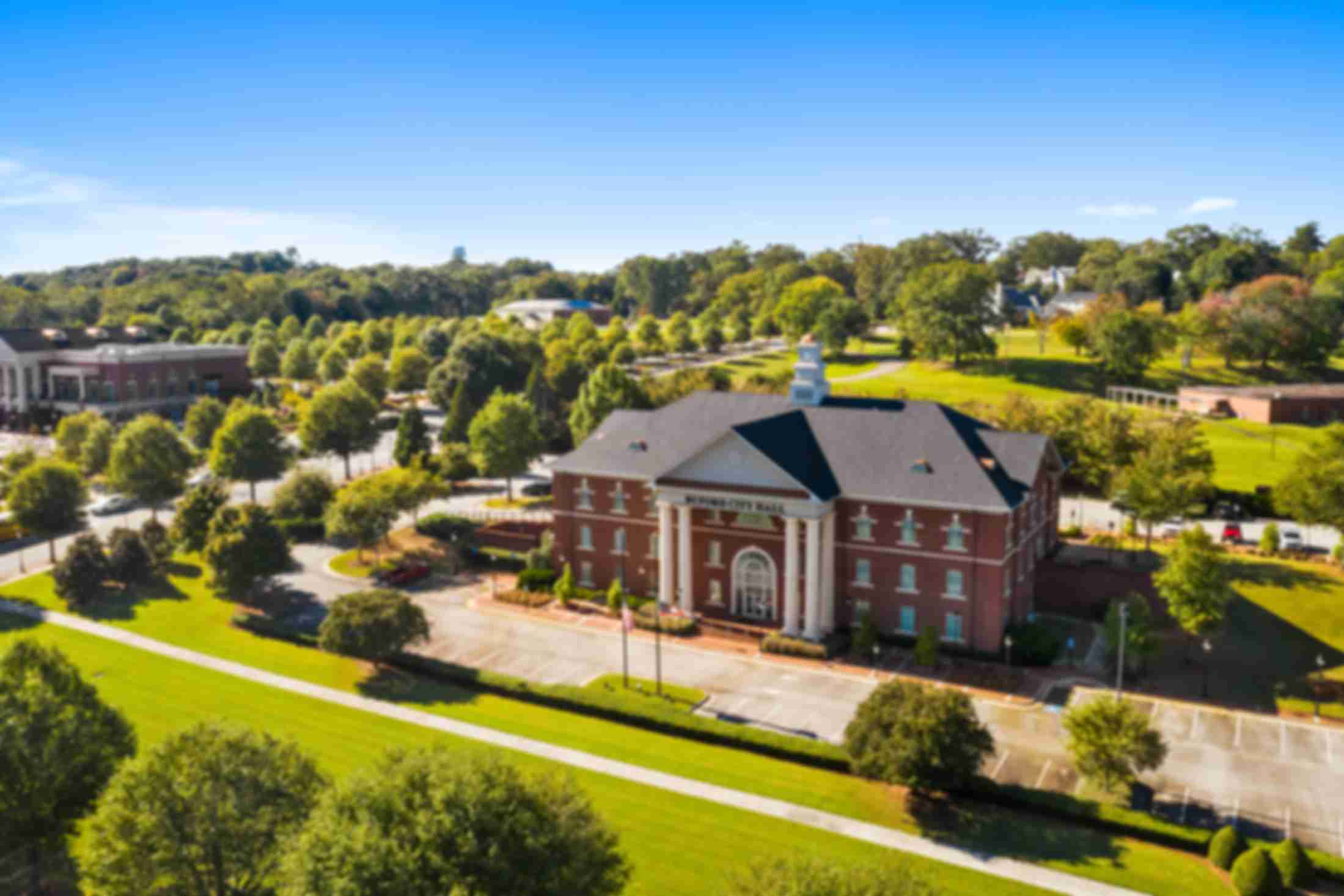 Aerial view of red brick clubhouse with clock tower at The Grove at East Thompson in Buford, Georgia, surrounded by trees and parking