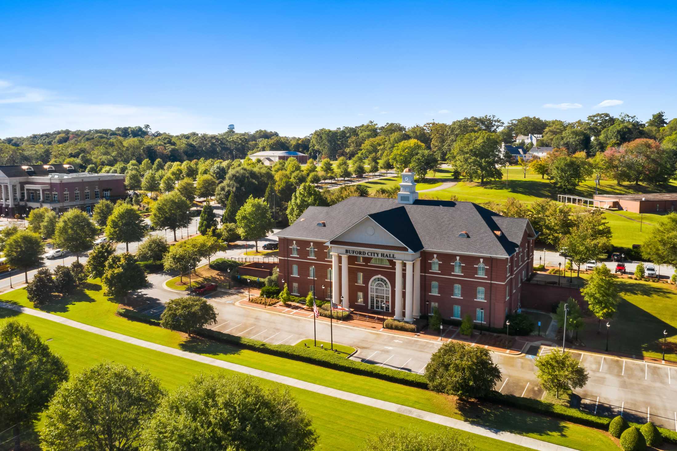 Aerial view of red brick clubhouse at Melody Lakeside Estates in Buford Georgia featuring columned entrance, lush trees, and parking areas