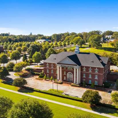 Aerial view of red brick clubhouse with clock tower at The Grove at East Thompson in Buford, Georgia, surrounded by trees and parking