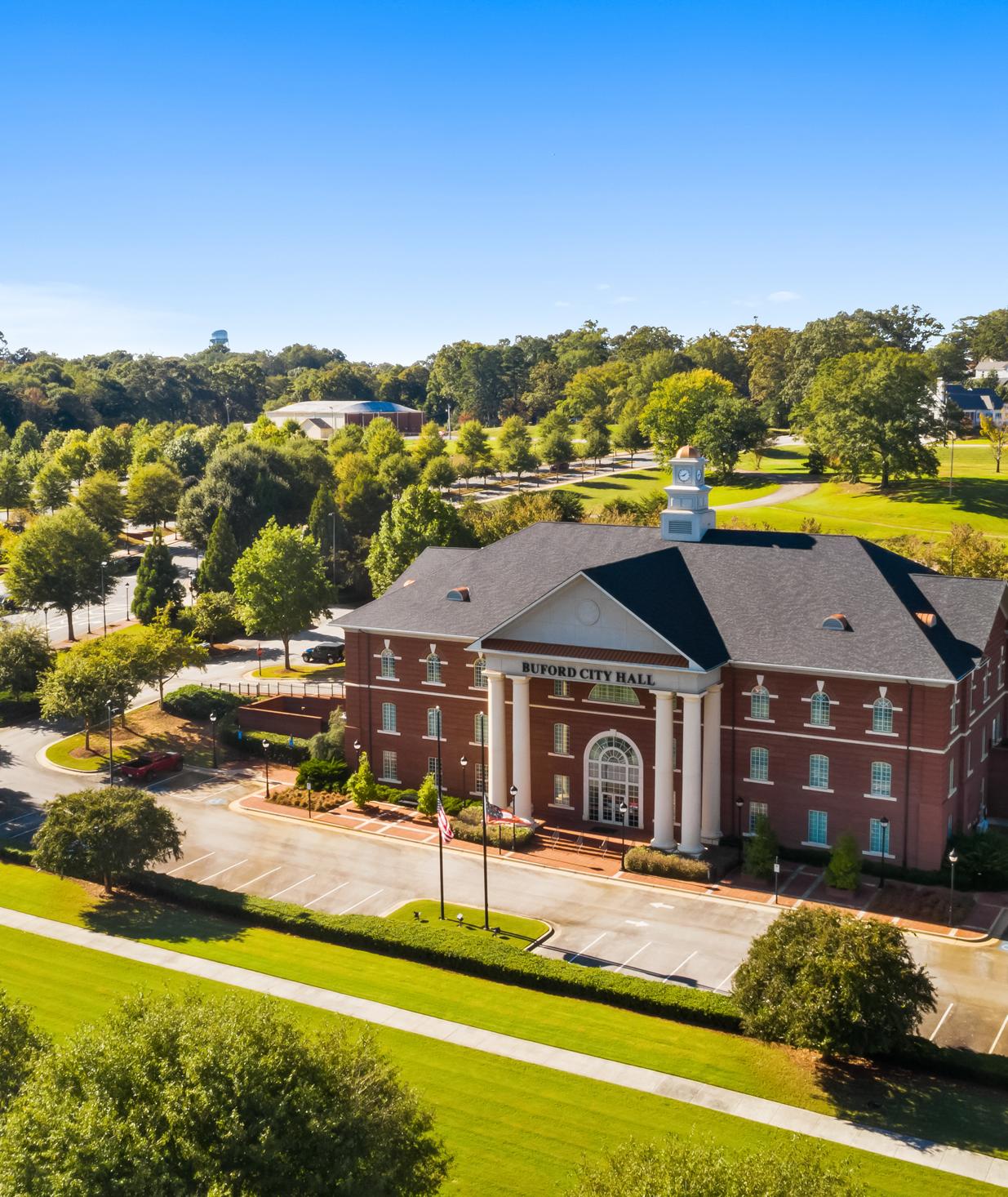 Aerial view of red brick clubhouse with clock tower at The Grove at East Thompson in Buford, Georgia, surrounded by trees and parking