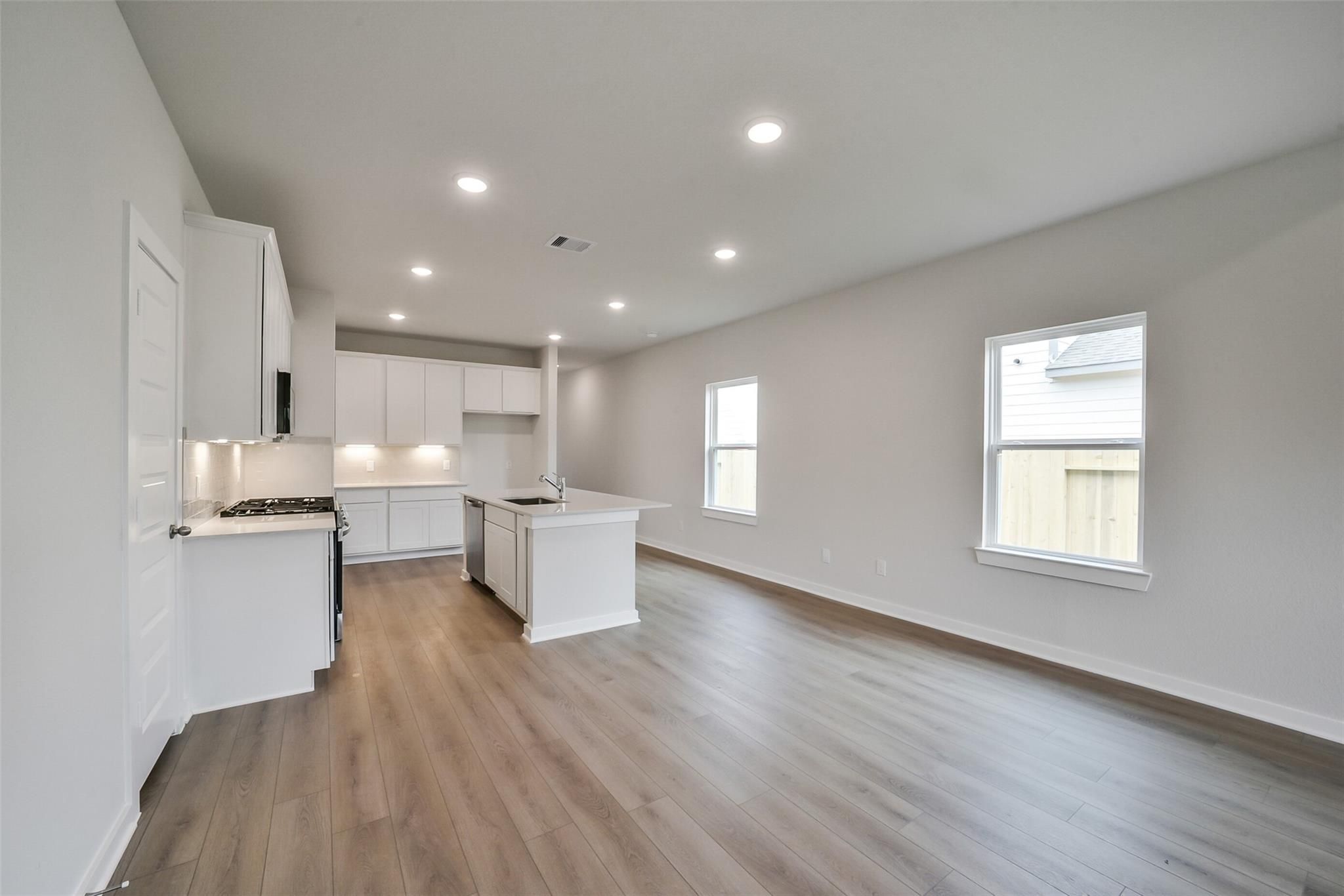 Bright open kitchen with white shaker cabinets, large island sink, stainless appliances, and wood floors in The Frio F, Conroe, Texas