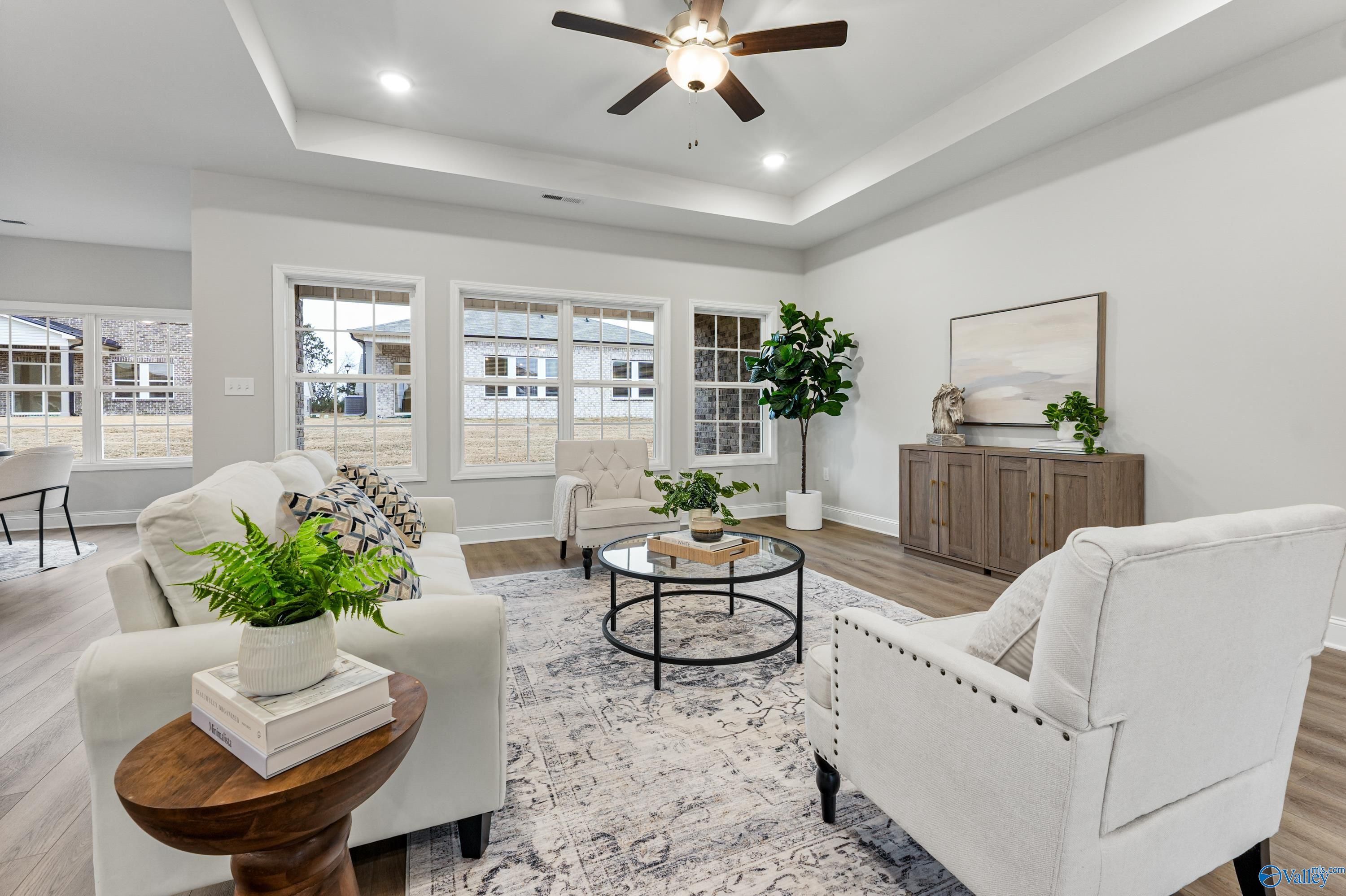 Cozy living room with white sofa, armchairs, plants, and large windows in Davidson Homes The Finleigh, Toney, Alabama